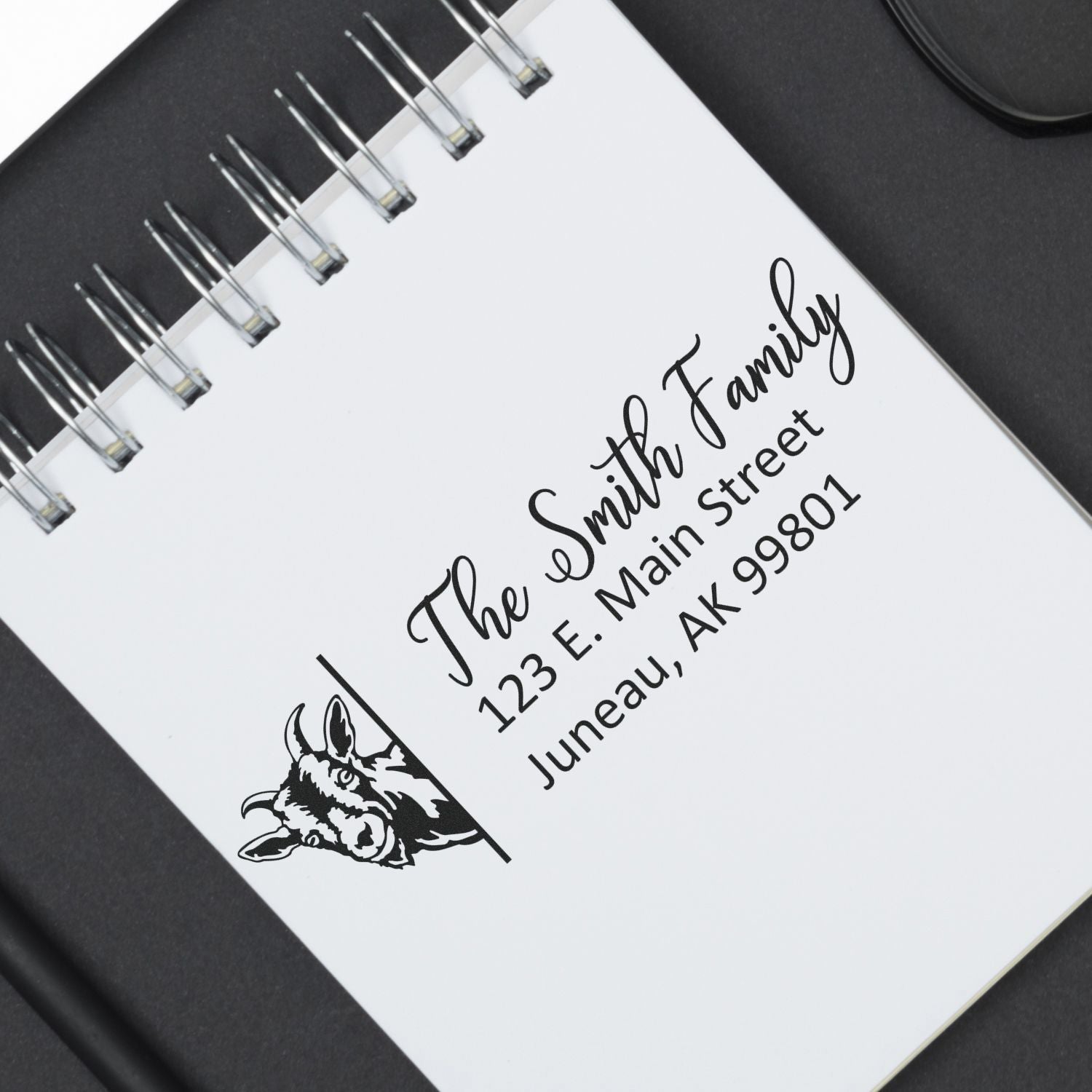 Personalized rubber address stamp for The Smith Family with goat logo, used on a spiral notebook.