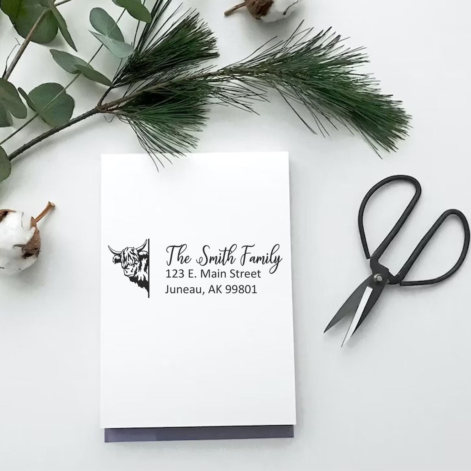 Custom return address rubber stamp with cow design on stationery, styled with greenery and scissors for personalized mailings.