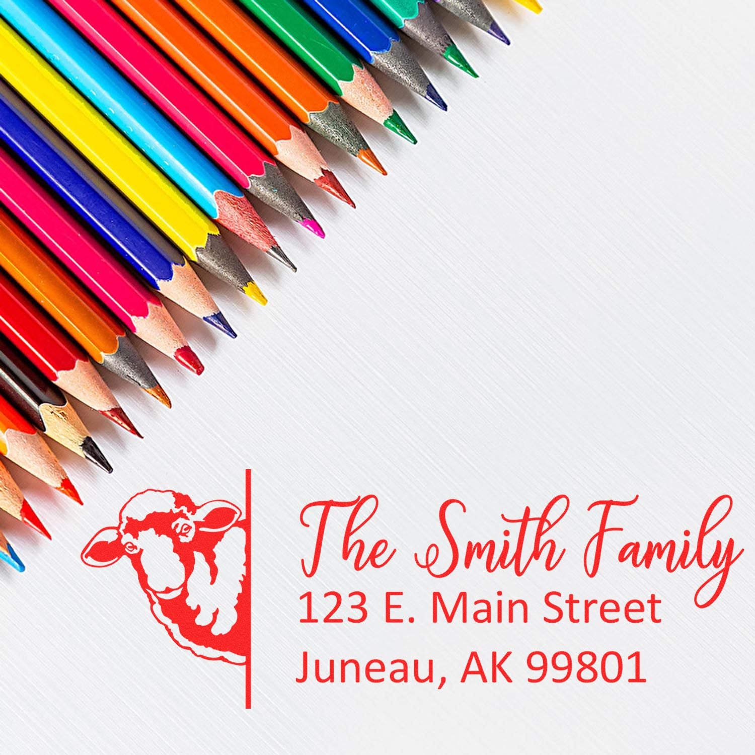 Custom rubber address stamp with sheep logo and family name, shown beside colorful pencils for personalized branding.