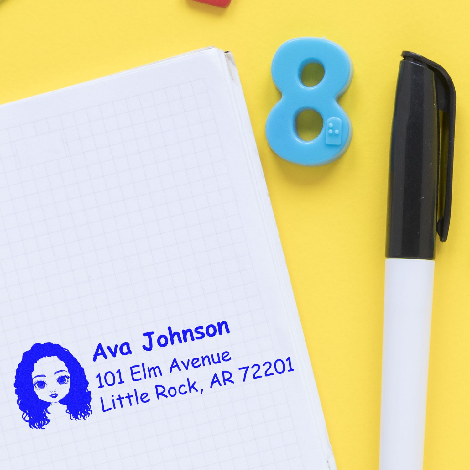 Personalized custom address rubber stamp impression on notebook, showing name and address with pen and number 8 on yellow background.