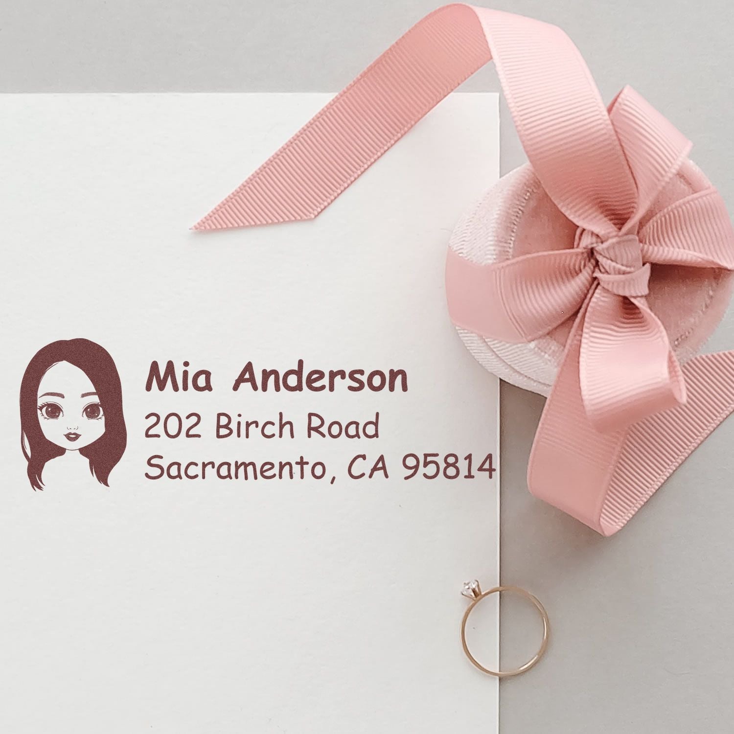 Personalized address rubber stamp on white envelope with pink ribbon, featuring name, address, and avatar design.