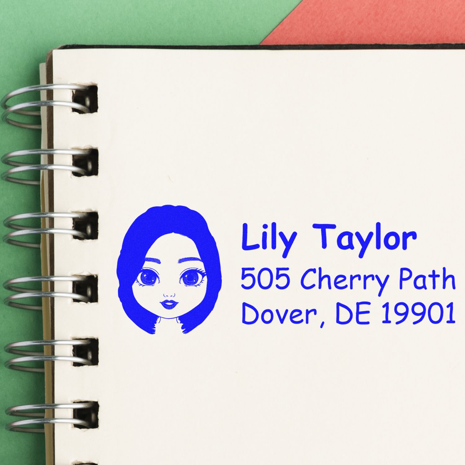 Custom rubber address stamp with girl avatar and Lily Taylor, 505 Cherry Path, Dover, DE 19901 on notebook page.