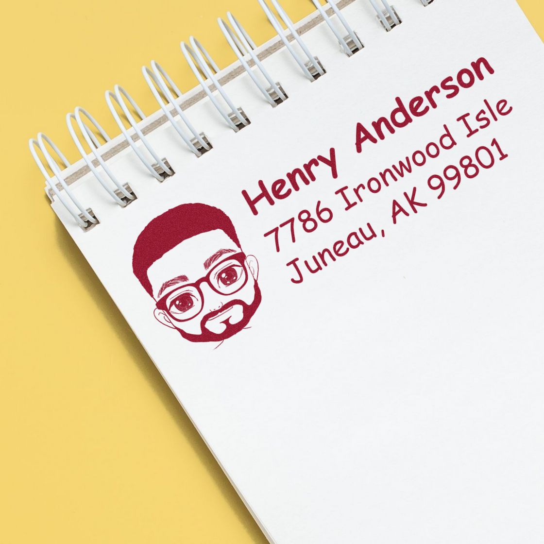 Personalized return address rubber stamp with portrait icon for Henry Anderson, Juneau, AK, on a spiral notebook.