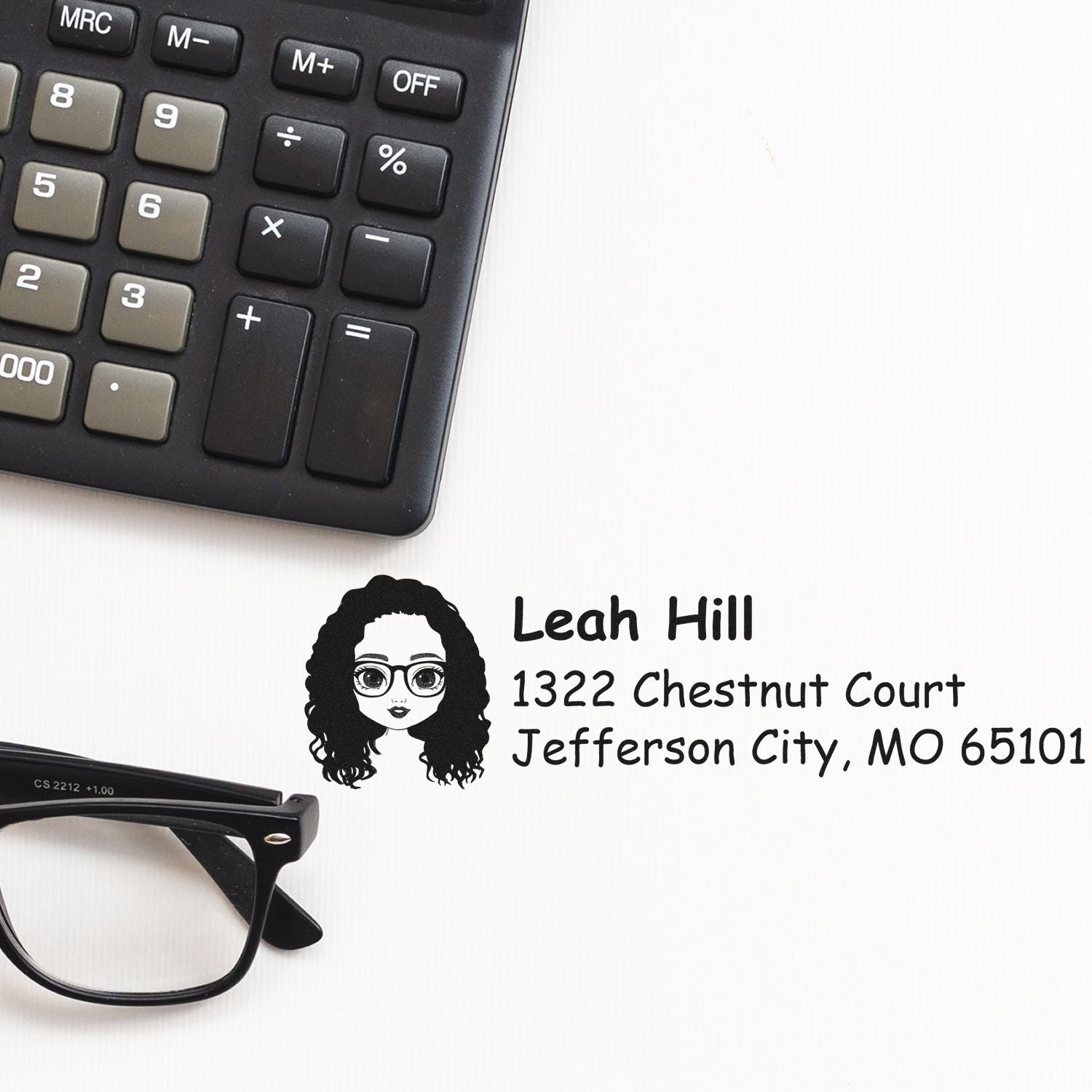 Custom address rubber stamp with name and address, shown beside a calculator and eyeglasses for office use.