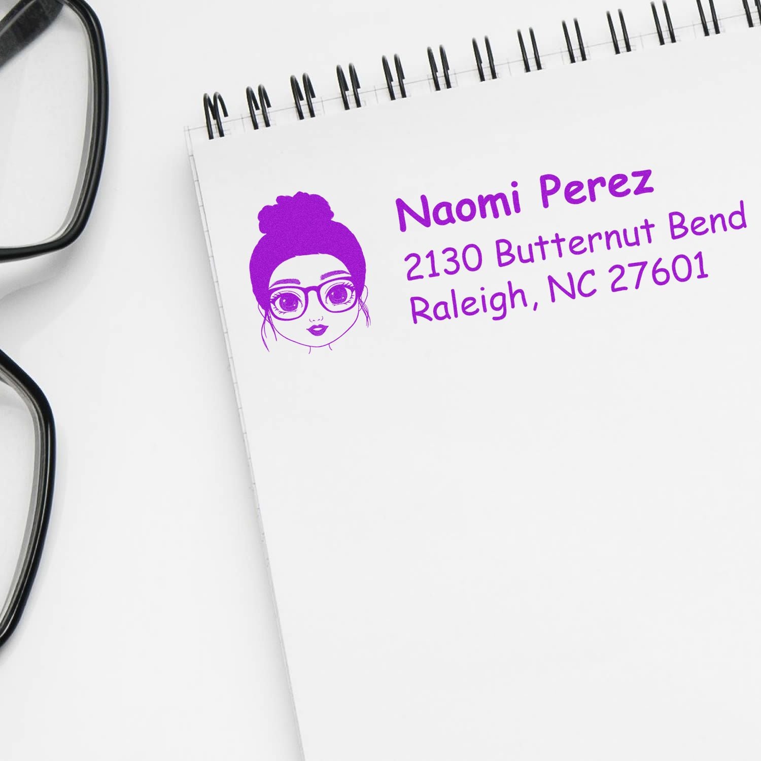 Custom rubber address stamp for mailing, featuring personalized name and address in purple ink on a notepad.