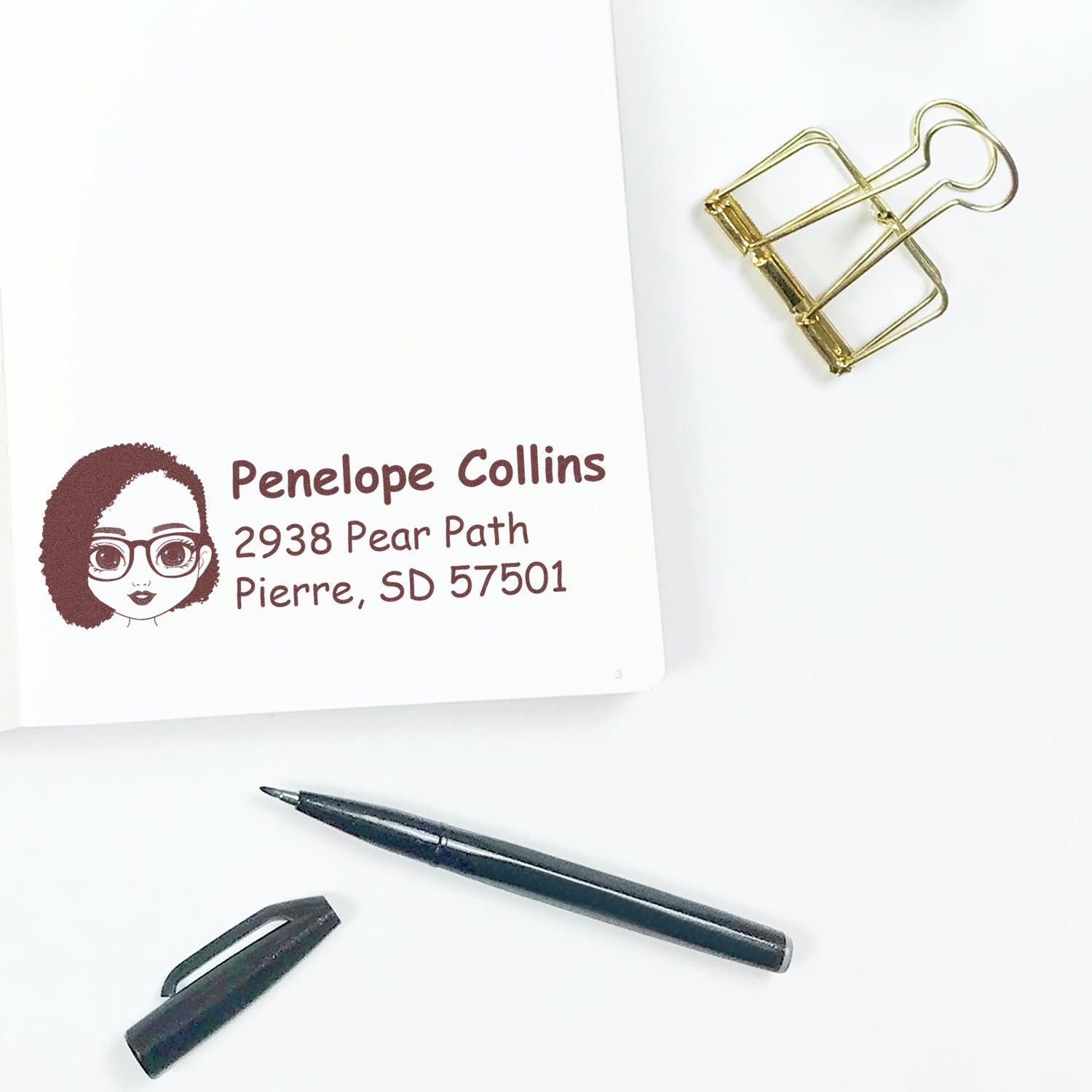 Personalized return address rubber stamp with custom name and address, shown on stationery with pen and binder clip.
