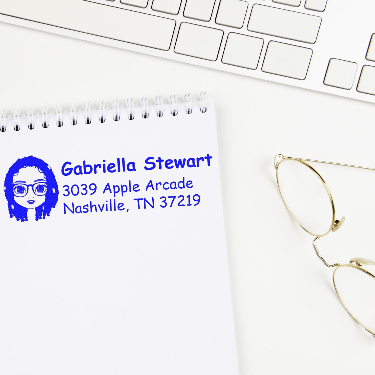 Personalized address rubber stamp with name and Nashville address stamped on notebook, beside keyboard and glasses.
