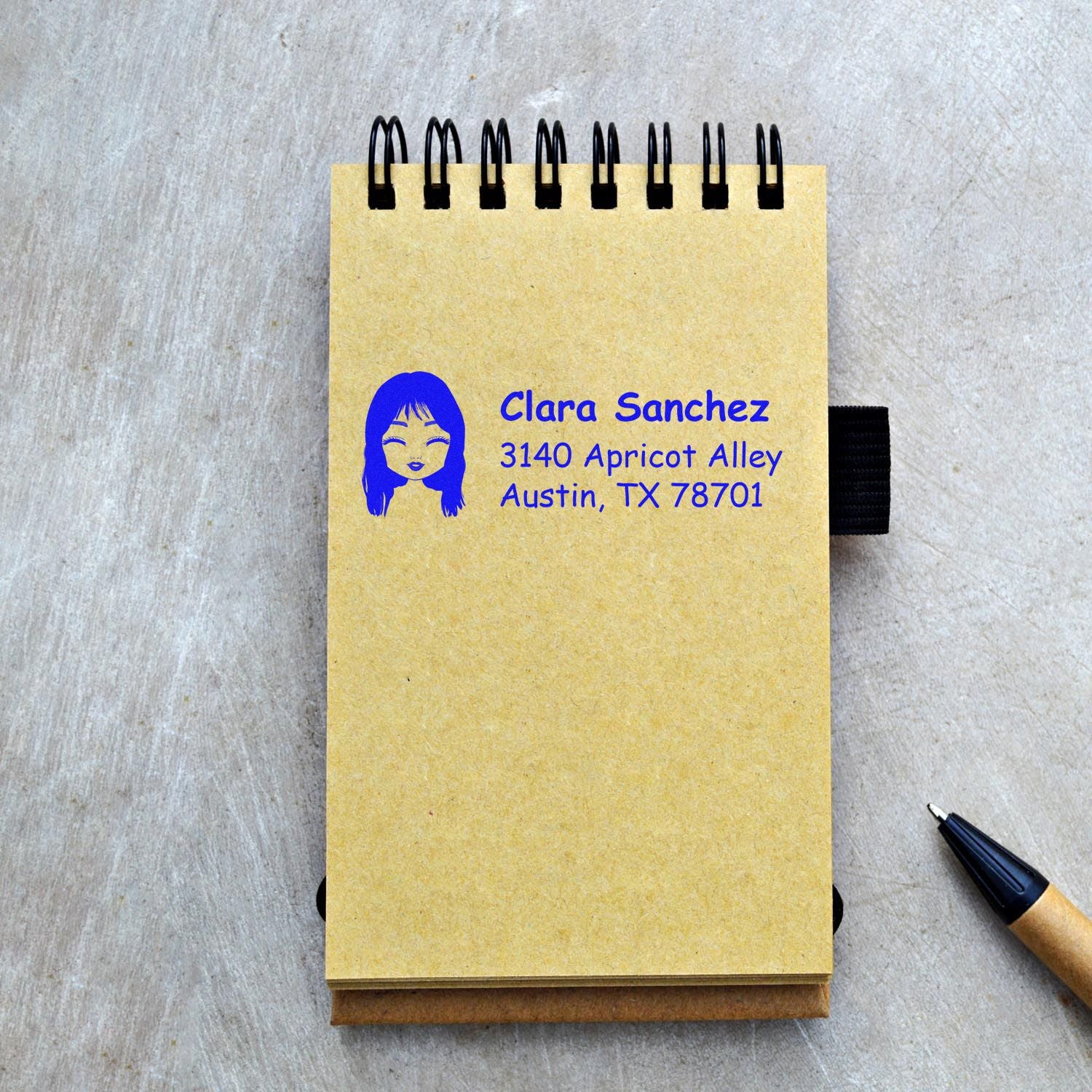 Custom return address rubber stamp with name, address, and portrait on notebook cover for personalized stationery.