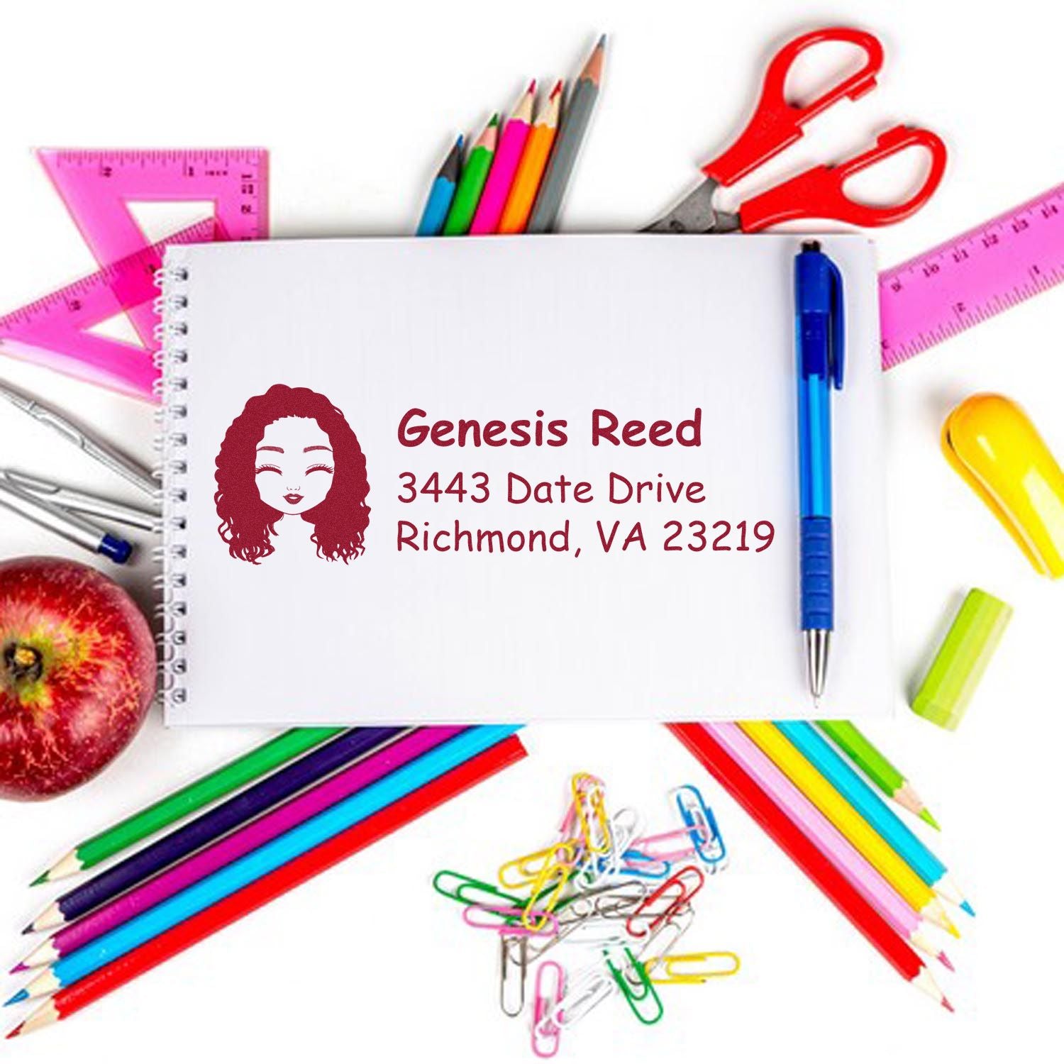 Custom return address rubber stamp with name and Richmond, VA address on a notebook surrounded by school supplies.
