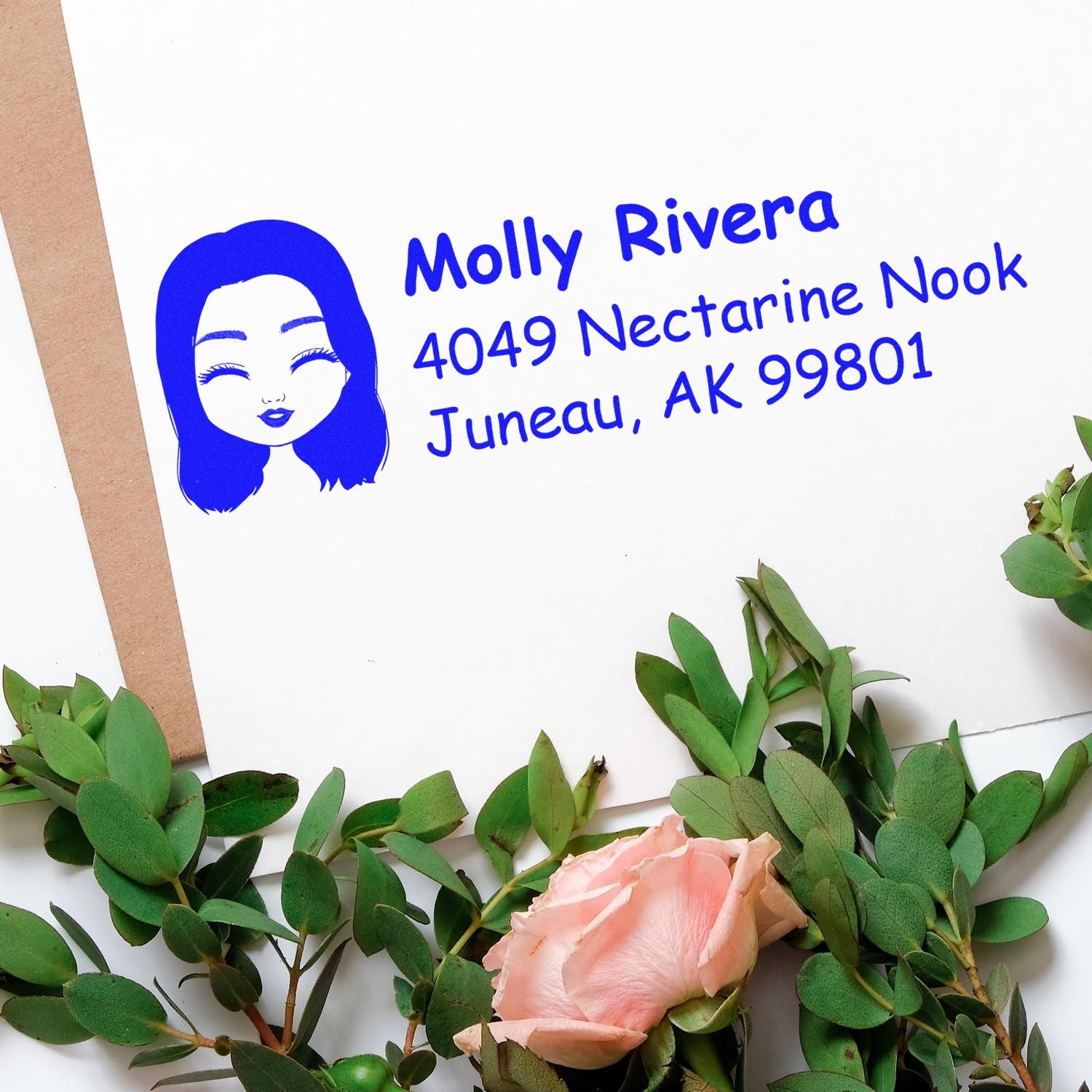 Personalized rubber address stamp with avatar design and return address, shown in blue ink on paper with floral styling.