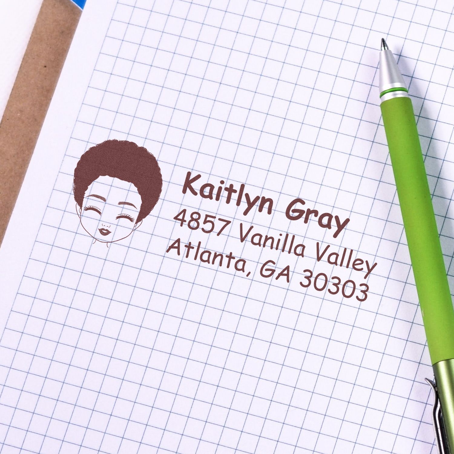 Custom return address stamp for Kathryn Gray, 4857 Vanilla Valley, Atlanta, GA 30303, shown on graph paper with a green pen.