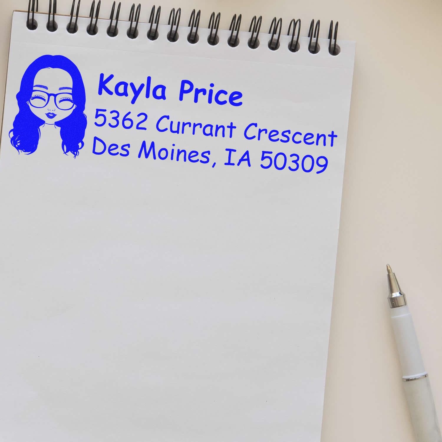 Personalized custom address rubber stamp with avatar logo, showing blue name and mailing address on notepad.