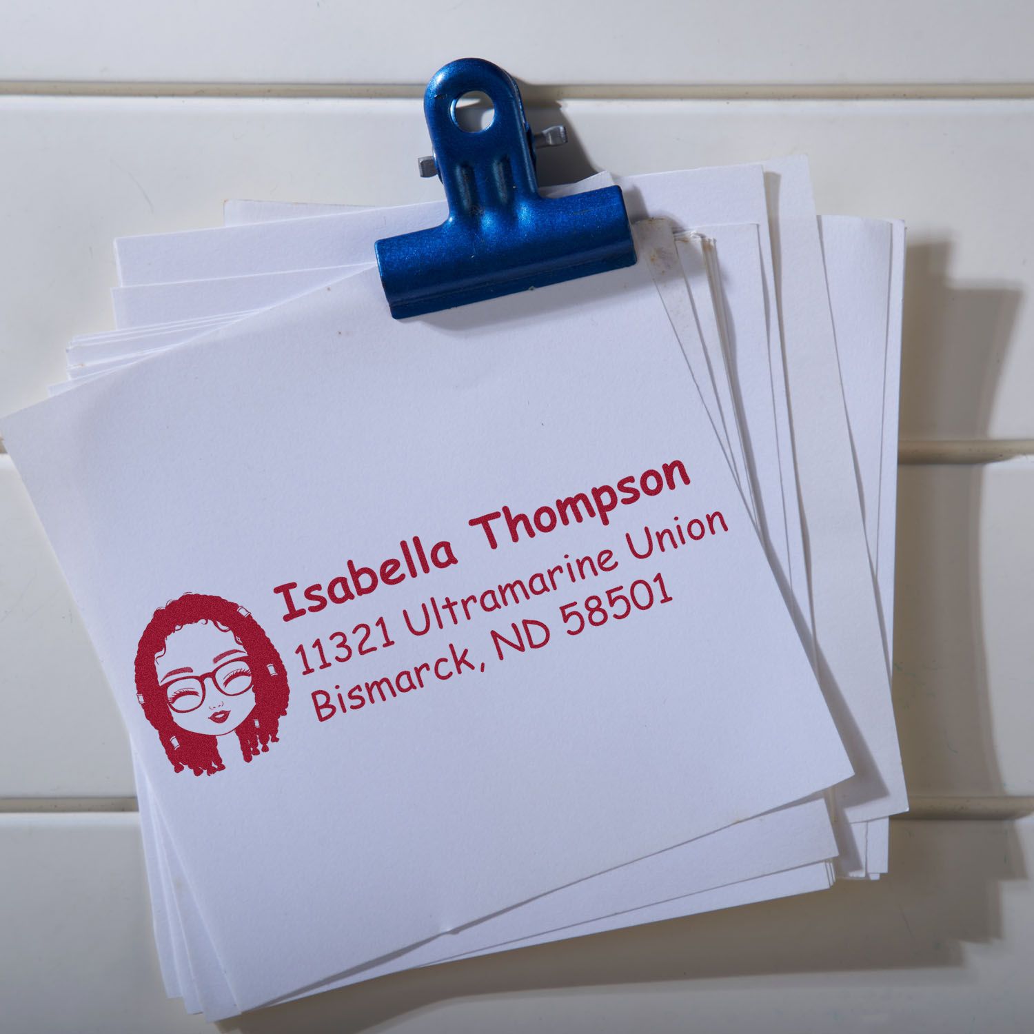 Custom return address rubber stamp on stacked paper, featuring a personalized name, address, and logo for mailing.
