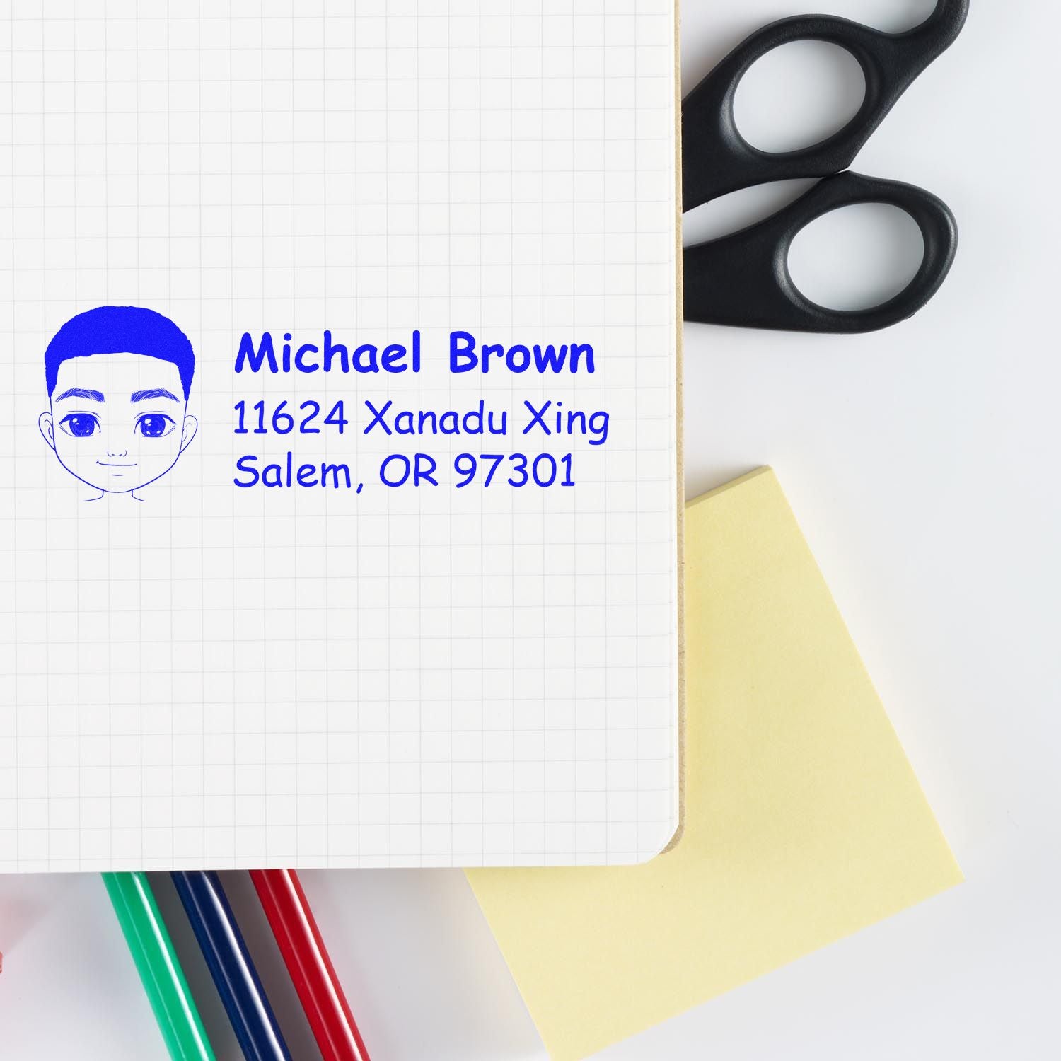 Personalized rubber address stamp design with name, street address and cartoon face on a notebook with stationery.