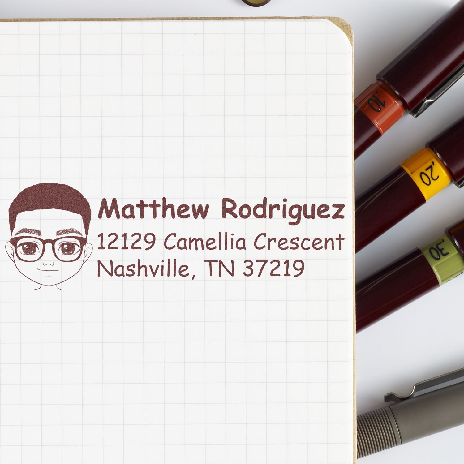 Custom rubber address stamp with portrait, Matthew Rodriguez return address for Nashville, TN, shown on notebook.