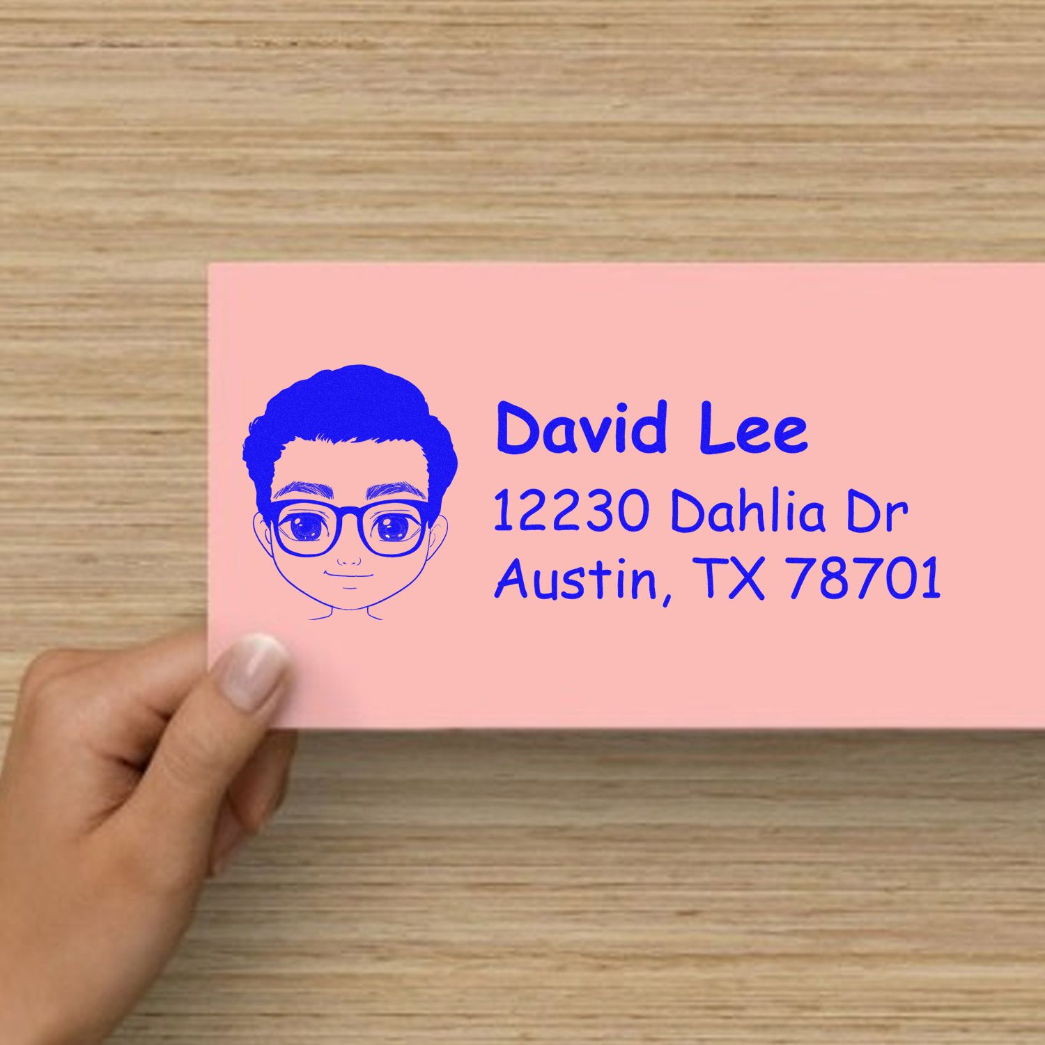 Custom rubber address stamp with cartoon portrait and return address for David Lee in Austin, TX on a pink envelope.
