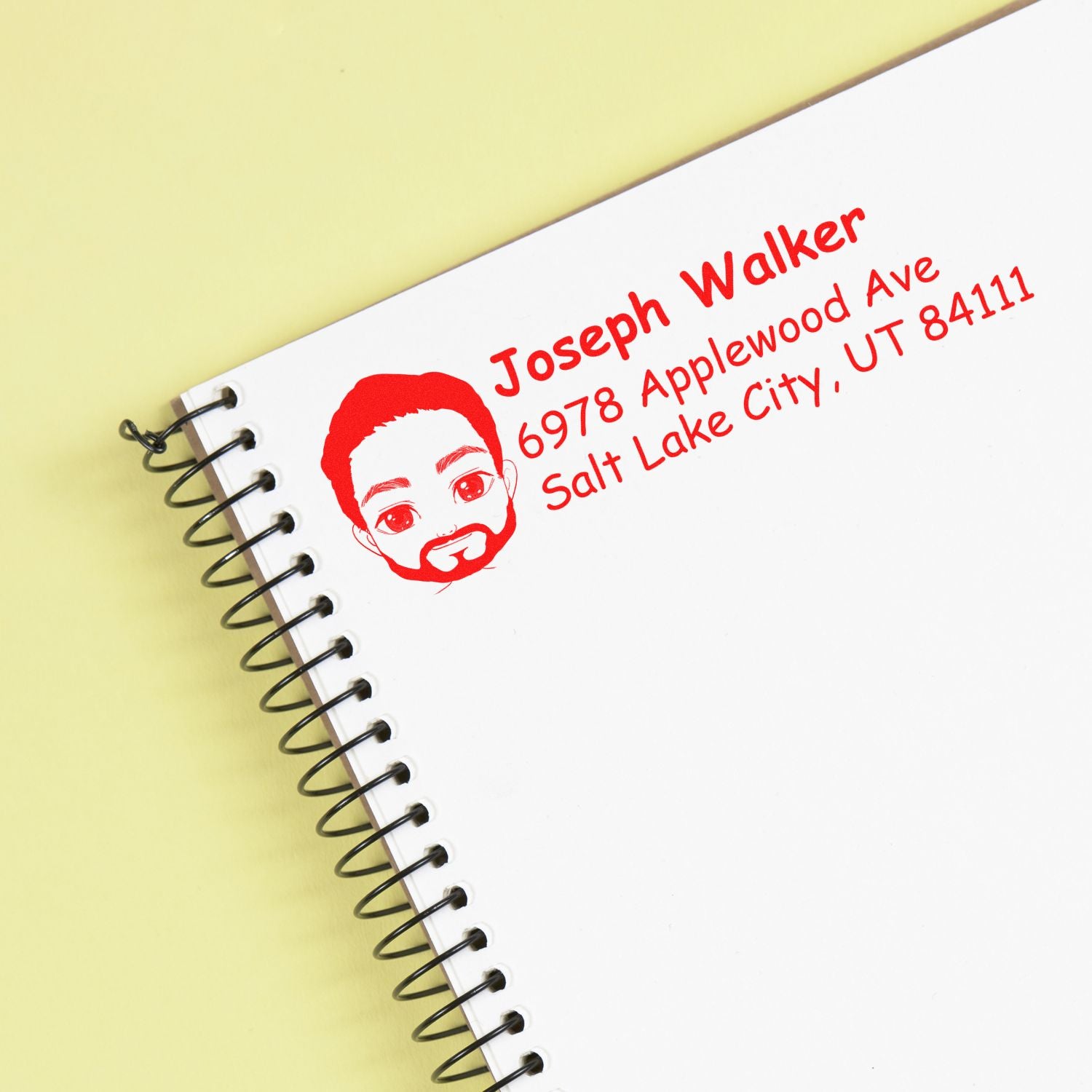 Personalized return address rubber stamp impression with name, Salt Lake City address, and avatar logo on a notebook.