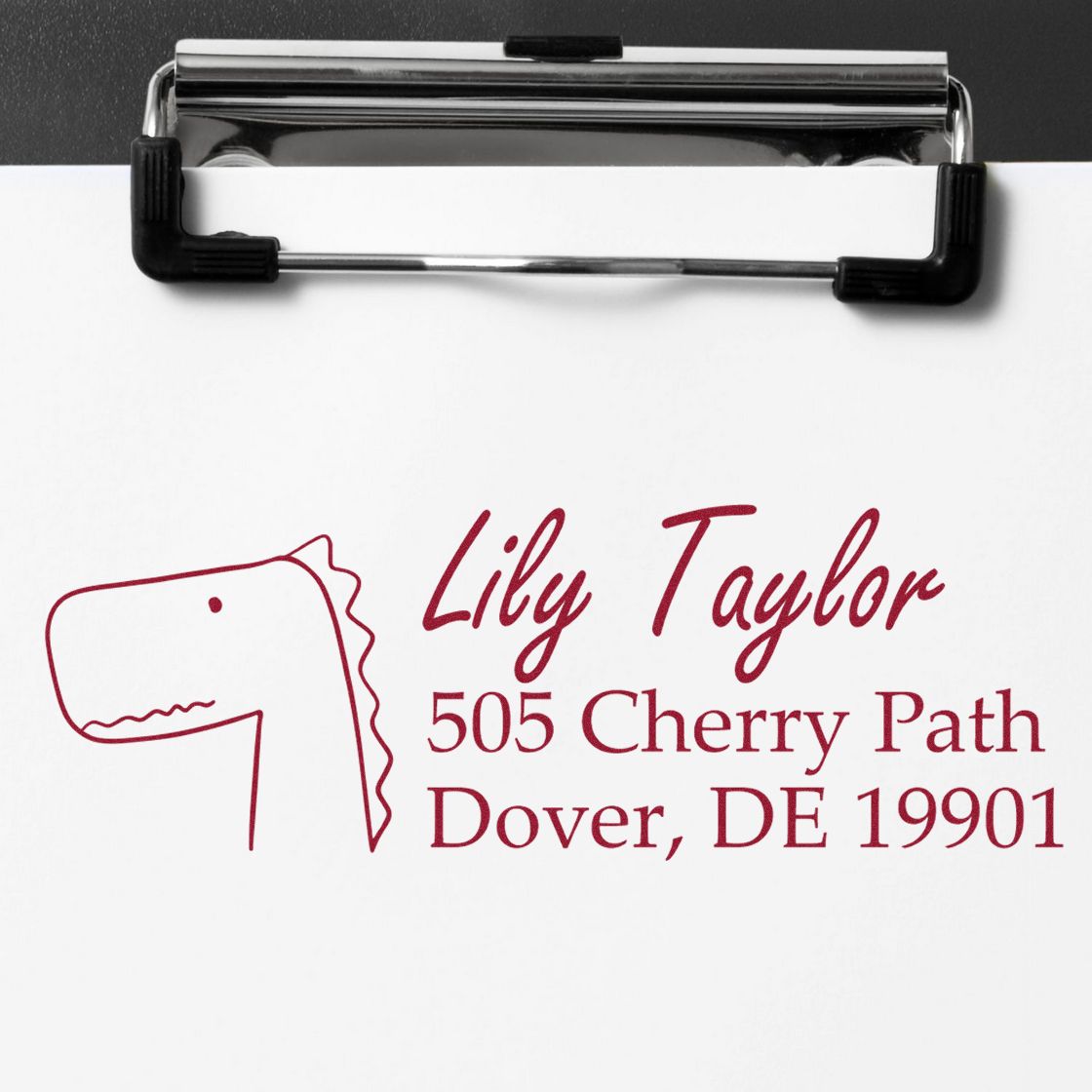 Custom return address rubber stamp with dinosaur logo, name, and mailing address for personalized envelopes.