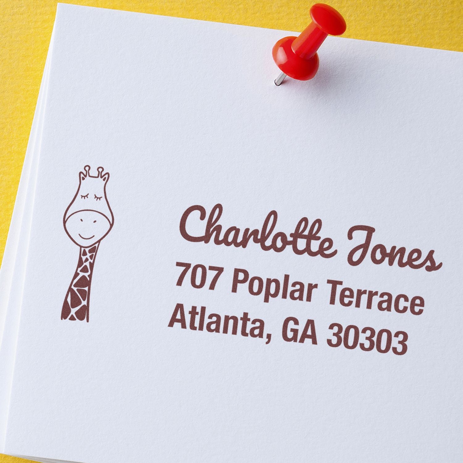 Custom rubber address stamp with giraffe logo for Charlotte Jones, Atlanta GA, on paper with red push pin.