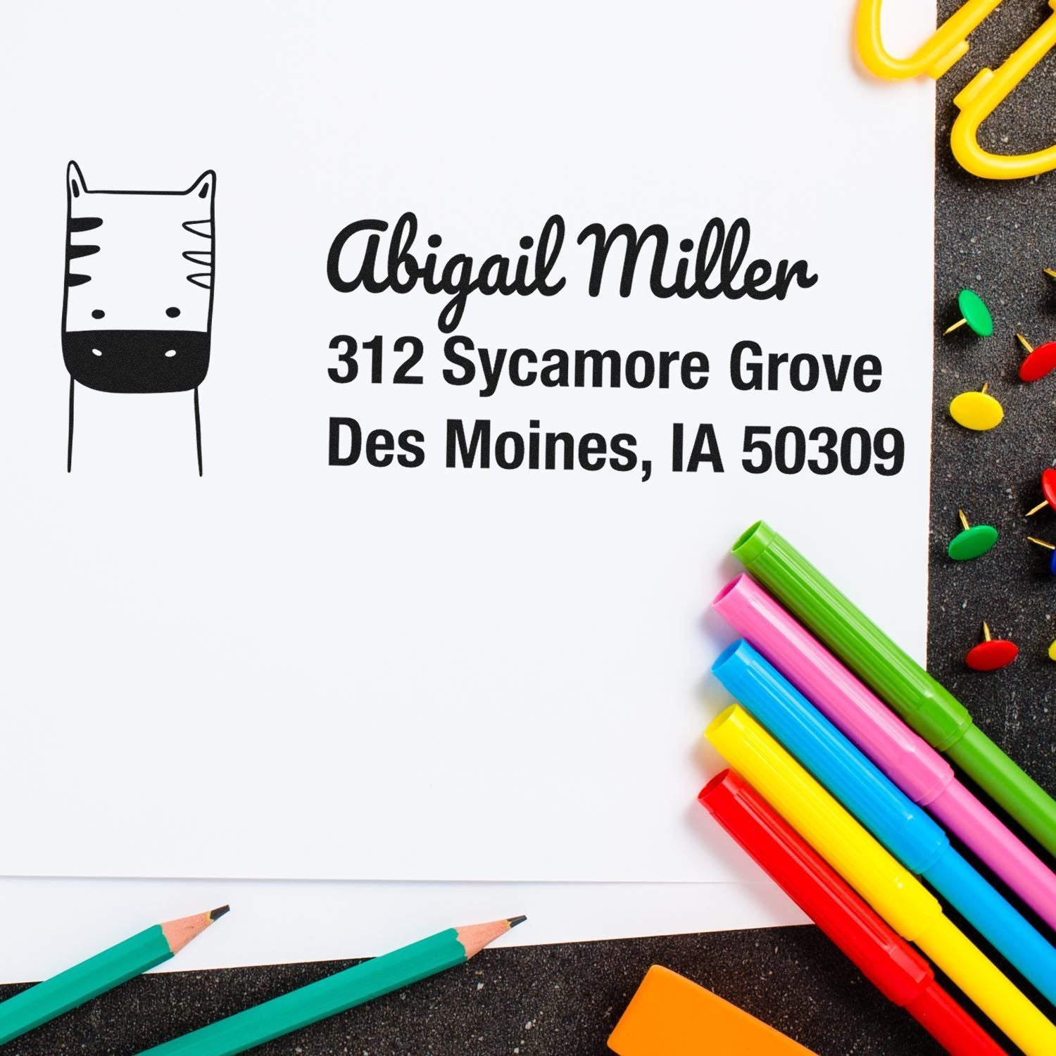 Custom cat return address rubber stamp with name and Des Moines, IA address, shown with colorful school supplies.