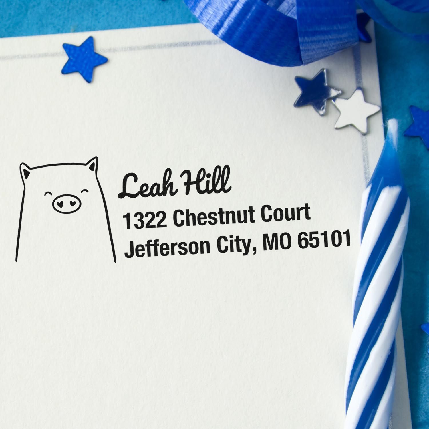 Custom rubber return address stamp with pig icon for Leah Hill, Jefferson City, MO, on festive blue stationery.