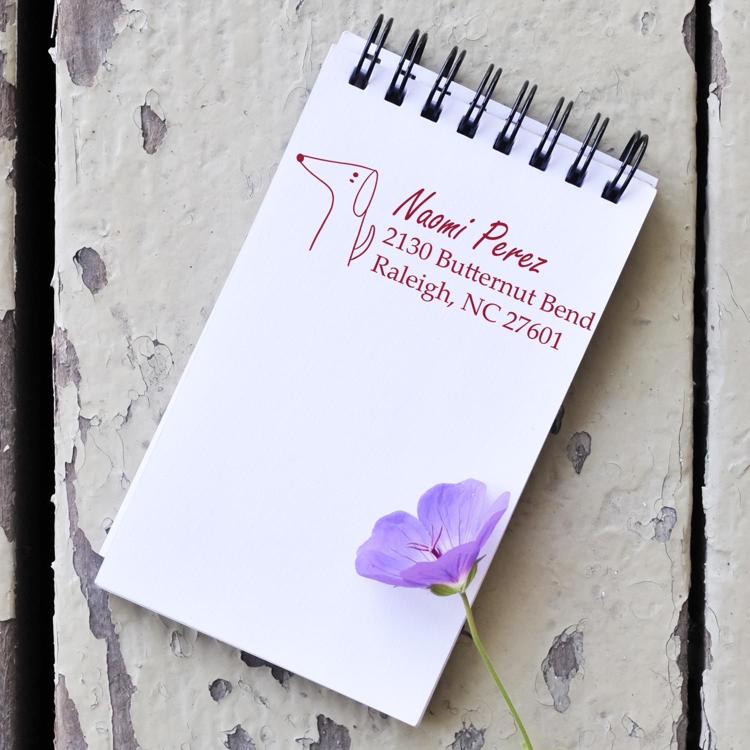 Personalized return address rubber stamp for Naomi Perez, Raleigh NC, shown on a spiral notepad with dog logo.