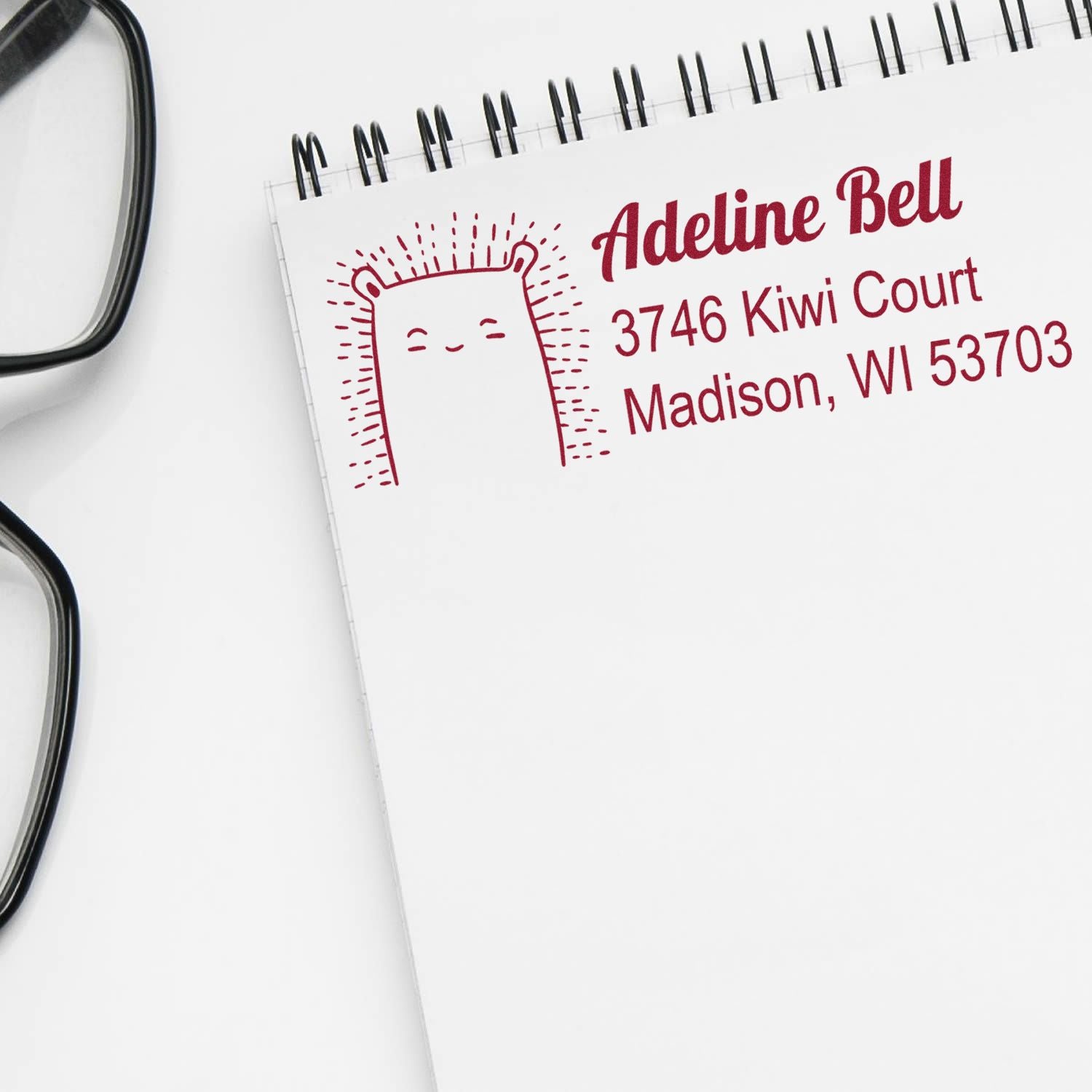 Personalized return address rubber stamp with cute bear design, showing Adeline Bell, Madison, WI 53703 on a notebook.