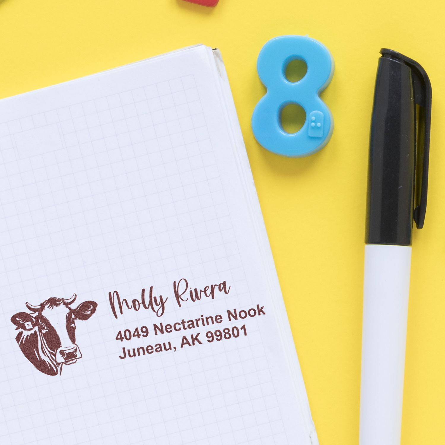 Custom address rubber stamp with cow logo on notebook, ideal for personalized return addresses and farmhouse business mailing.