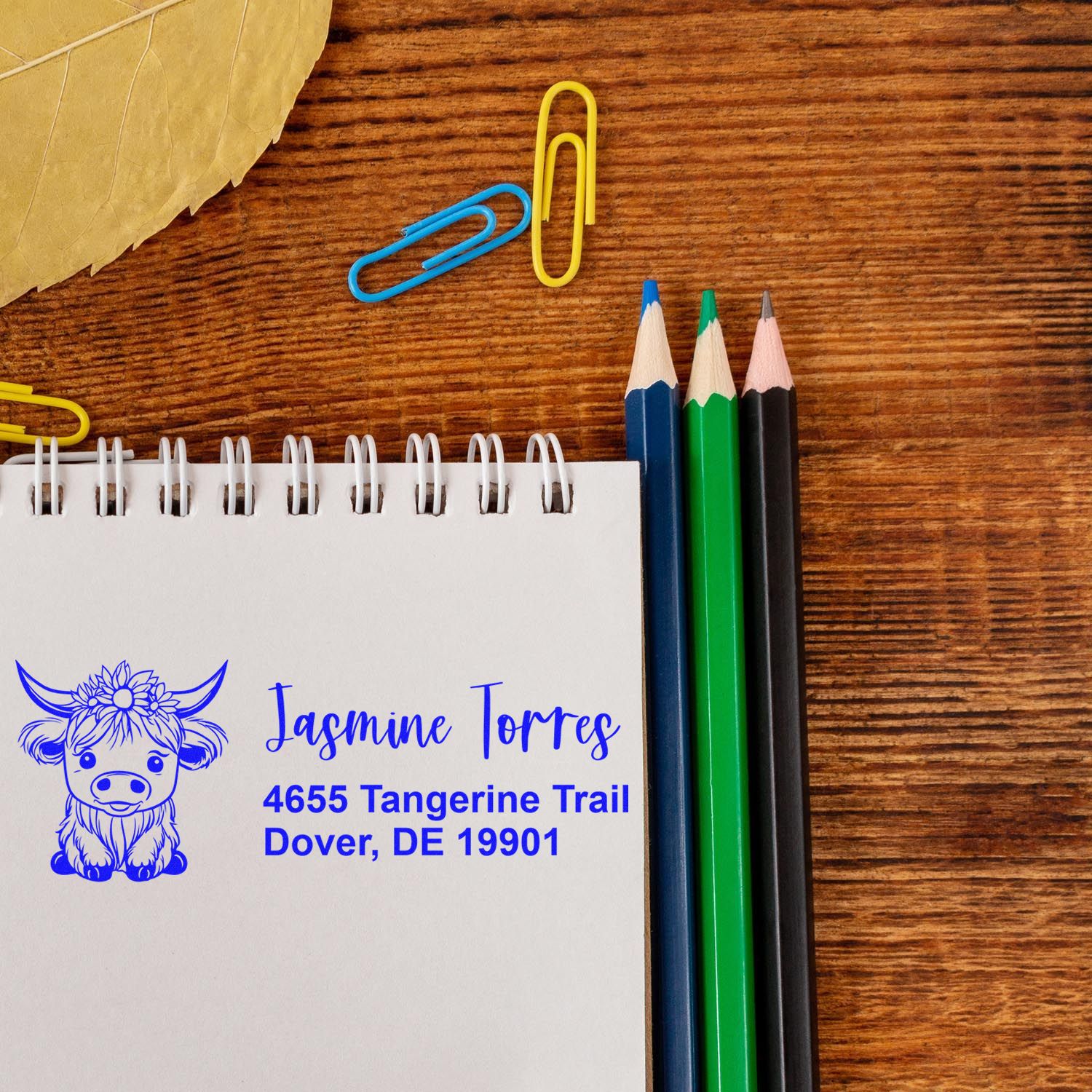 Custom return address rubber stamp with cow design and personalized name and address on notebook beside pencils.