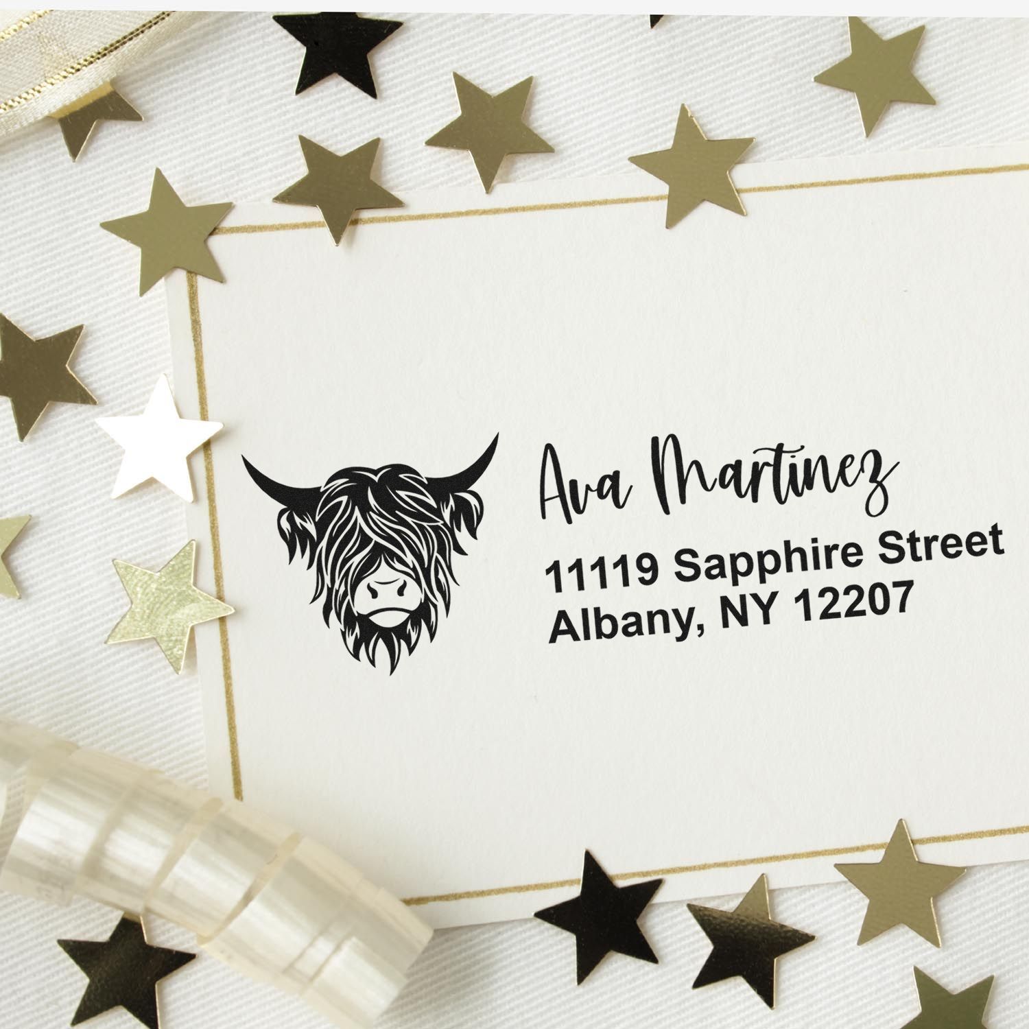 Custom Highland cow address rubber stamp on a white envelope with gold star confetti for personalized mailing.
