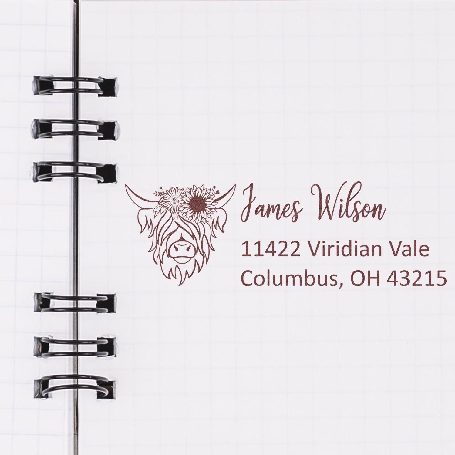 Personalized custom rubber address stamp with floral cow logo, James Wilson name, and Columbus, OH address on notebook paper.