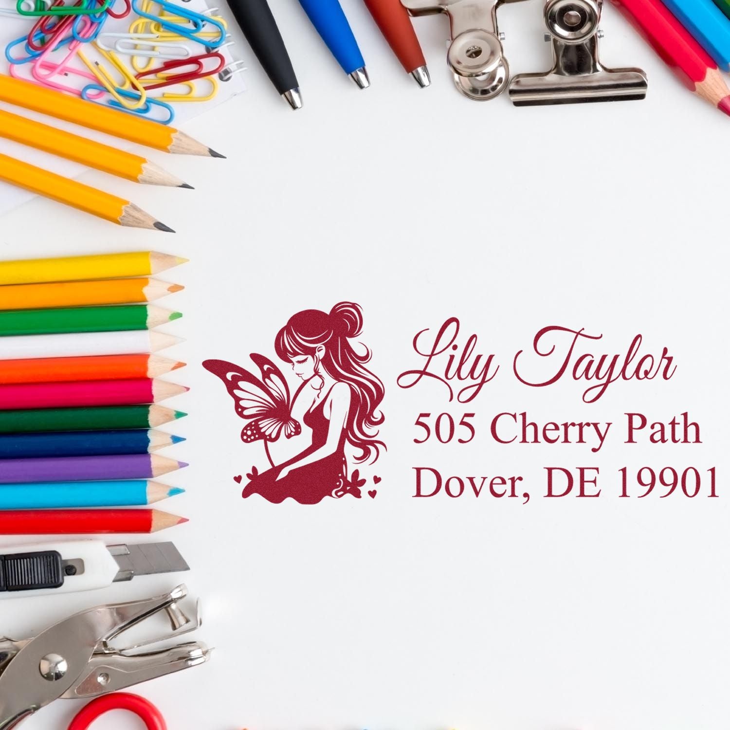 Personalized rubber stamp with fairy logo and Lily Taylor address, surrounded by pencils and office supplies for custom stationery.
