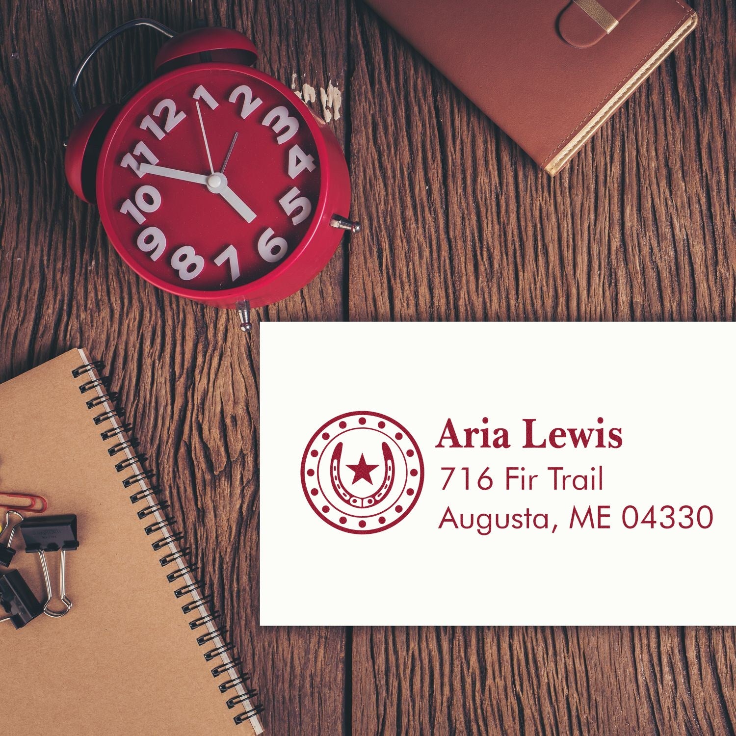 Personalized address rubber stamp for Aria Lewis, 716 Fir Trail, Augusta, ME 04330, displayed with stationery on a wood desk.