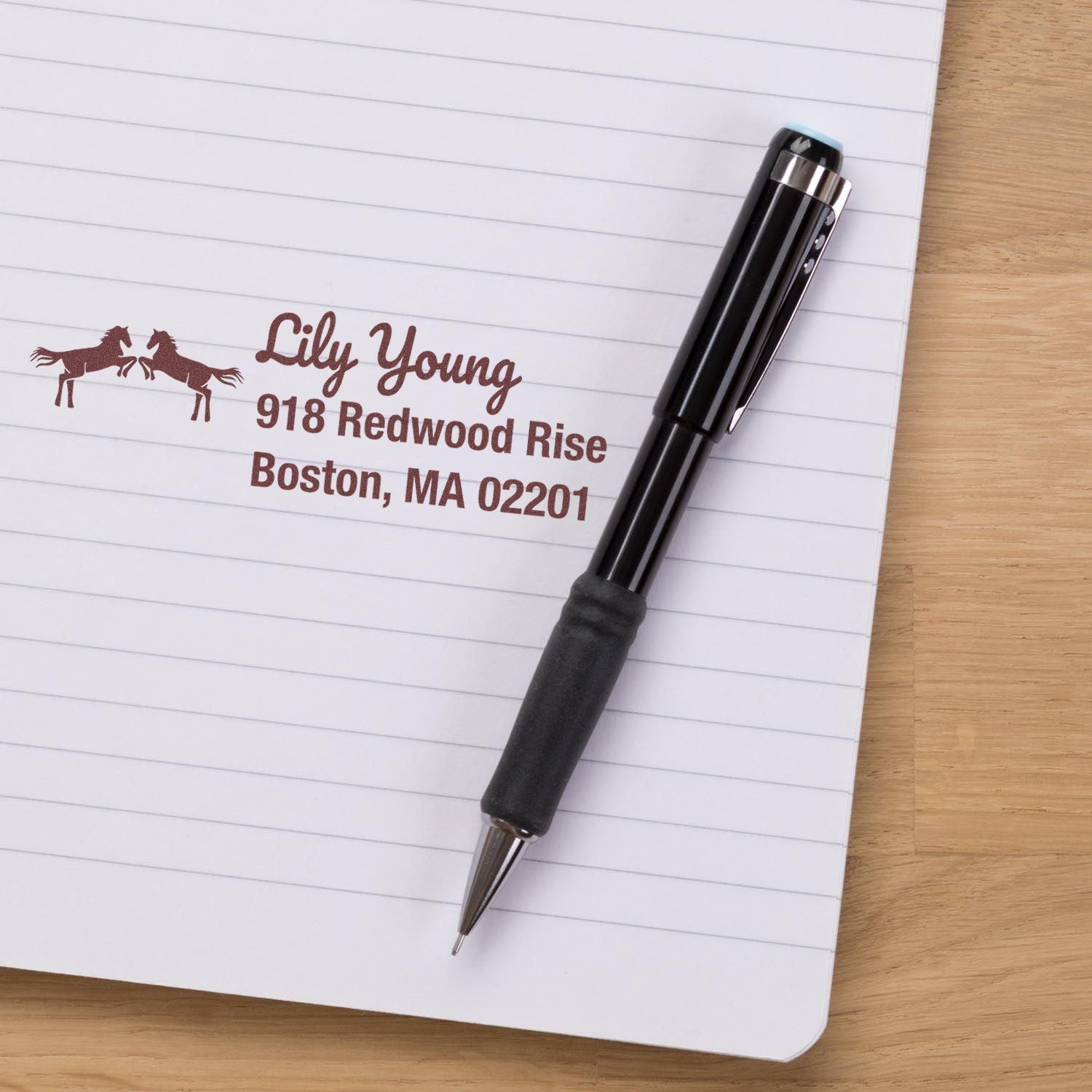 Custom self-inking rubber address stamp with horse design, showing Lily Young return address on notebook paper.