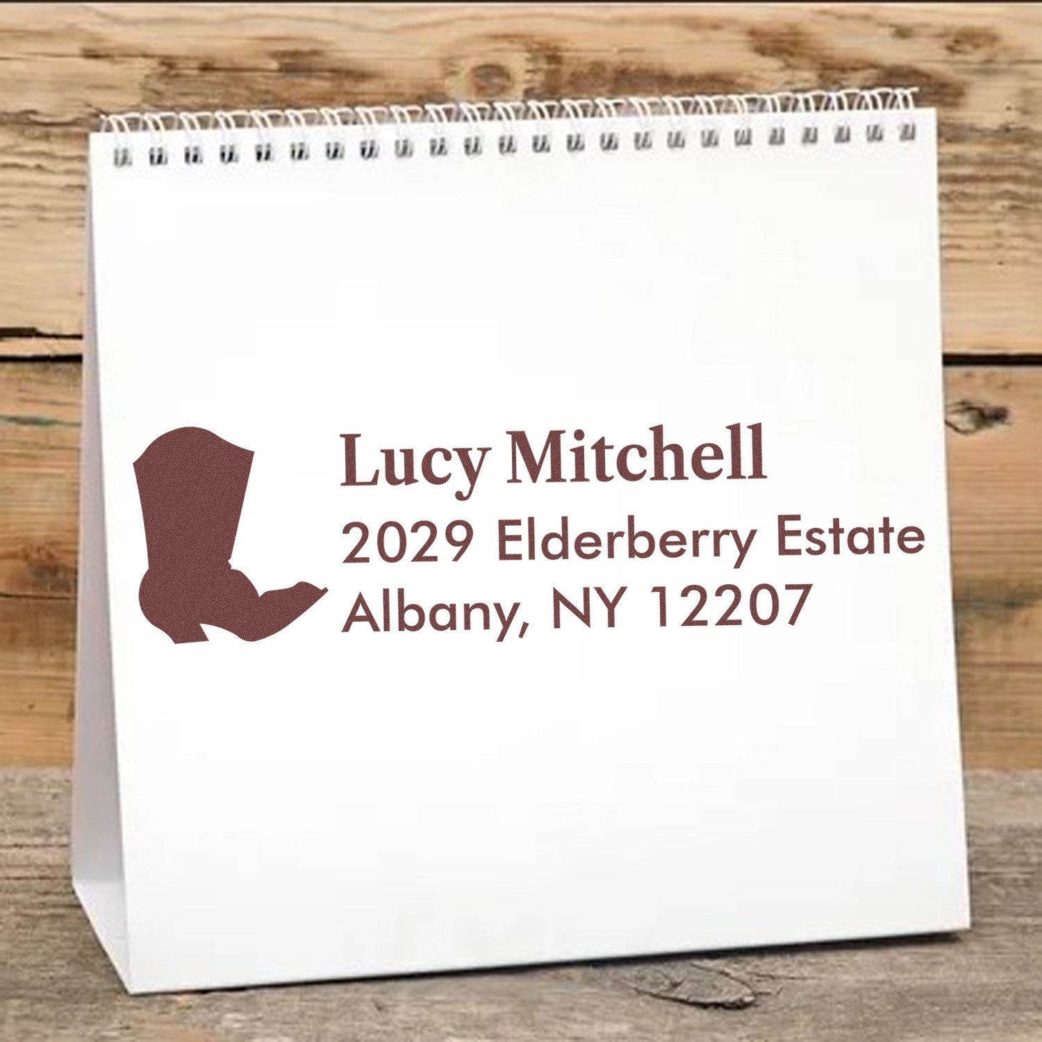 Custom return address rubber stamp with boot design for Lucy Mitchell, Albany, NY 12207 on a white paper bag