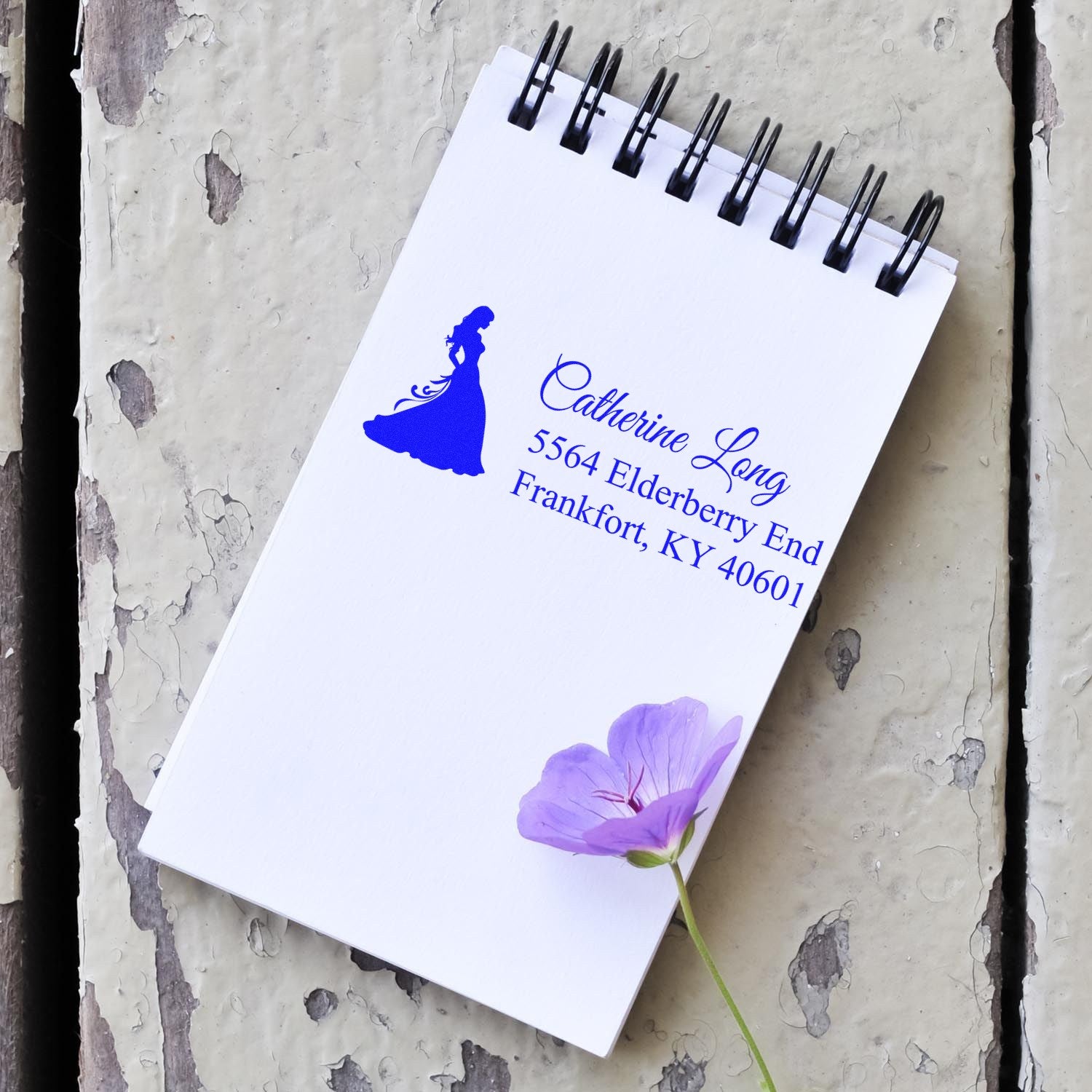 Custom rubber stamp impression with woman silhouette, name, and return address on a spiral notepad, ideal for wedding or mailing.