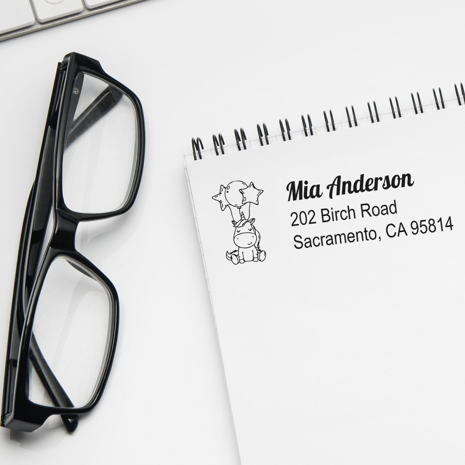 Custom return address rubber stamp with unicorn design on notebook, beside eyeglasses, for personalized stationery.