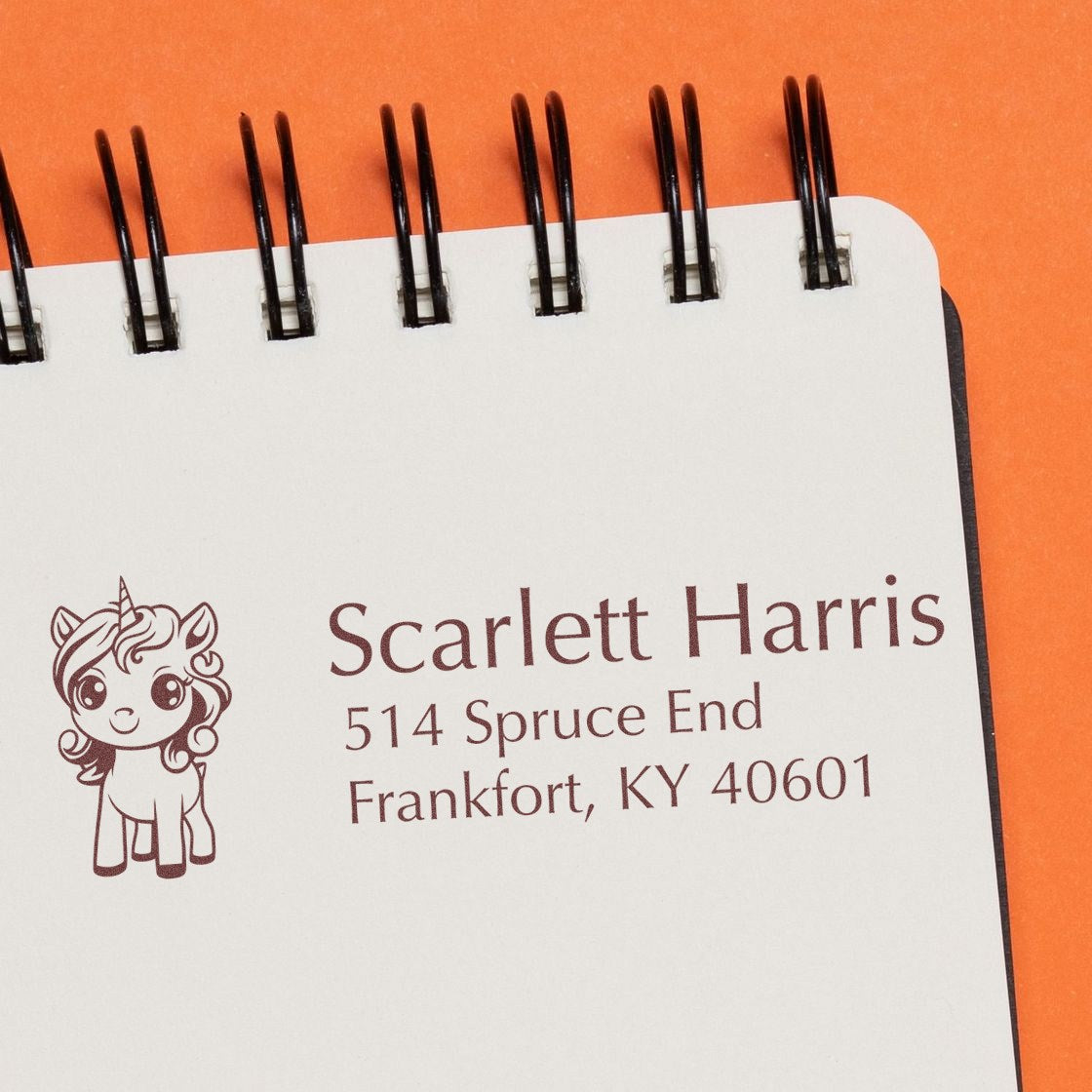 Personalized unicorn return address rubber stamp for Scarlett Harris, Frankfort, KY, on a notebook page.