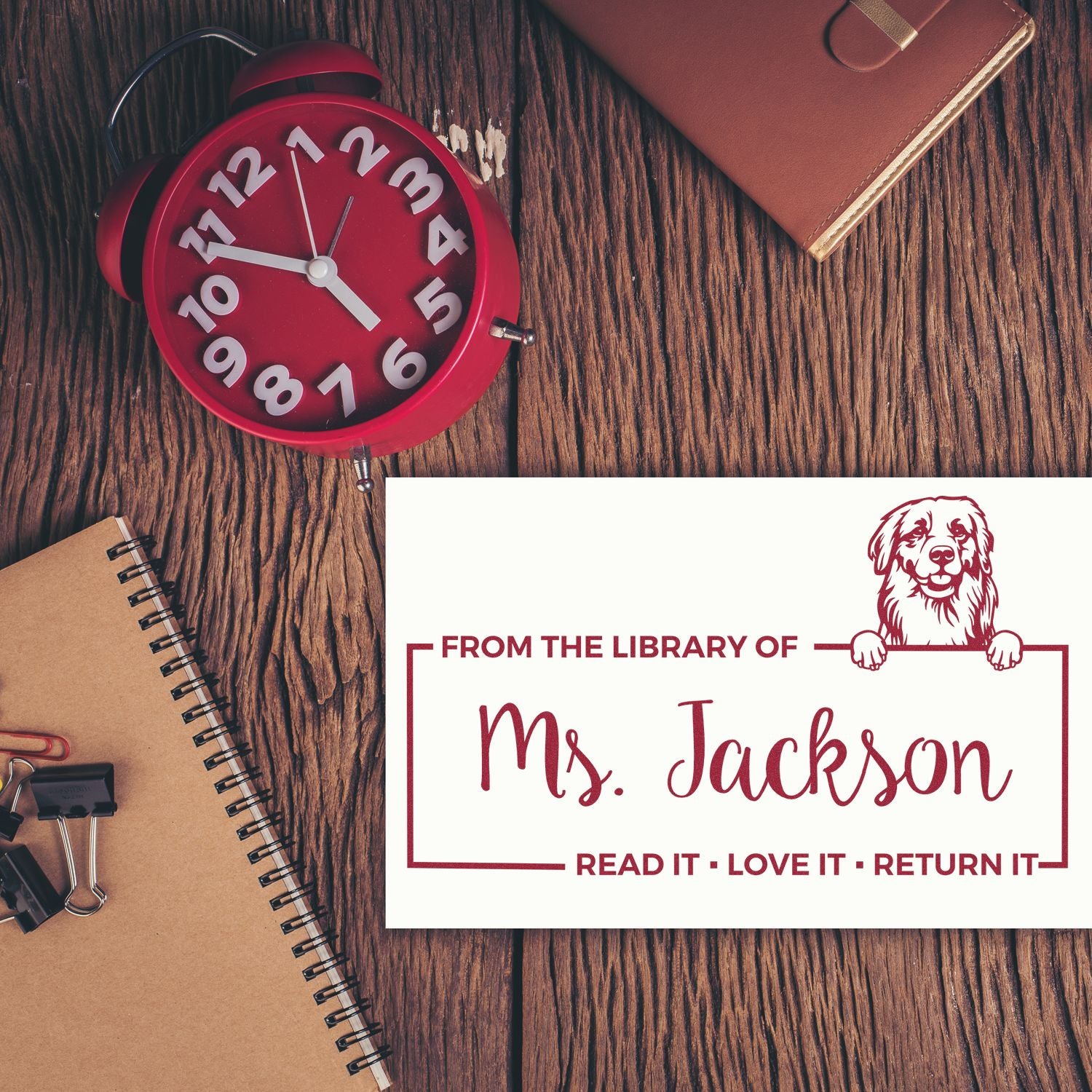 Personalized library rubber stamp for Ms. Jackson with dog logo and Read it, love it, return it message on a desk.