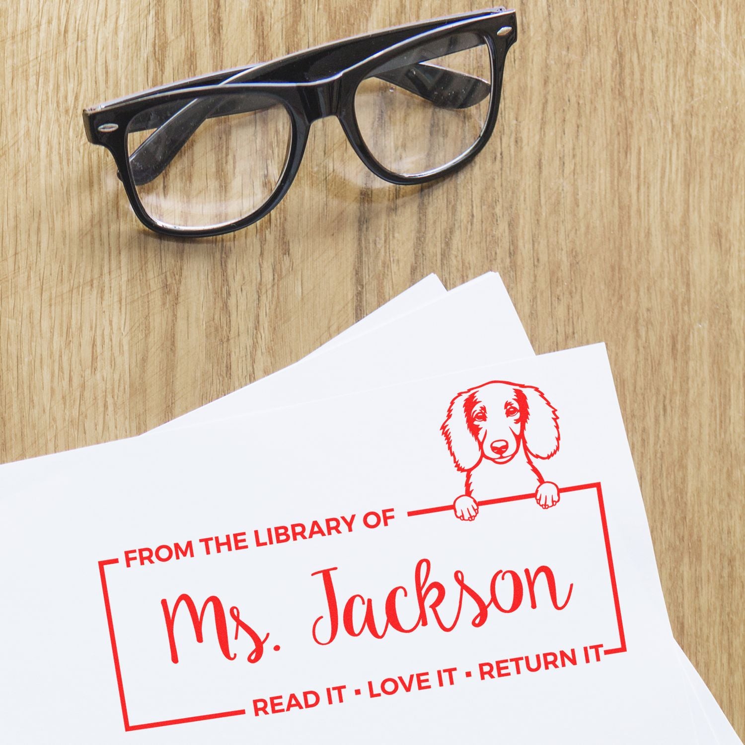 Custom library return rubber stamp for Ms. Jackson with dog design on paper beside eyeglasses.