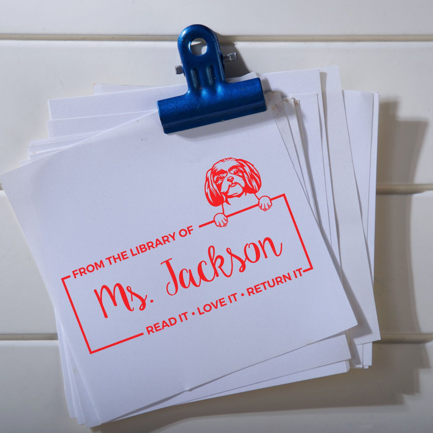 Personalized library rubber stamp on paper stack, reading From the Library of Ms. JacksonRead It, Love It, Return It.