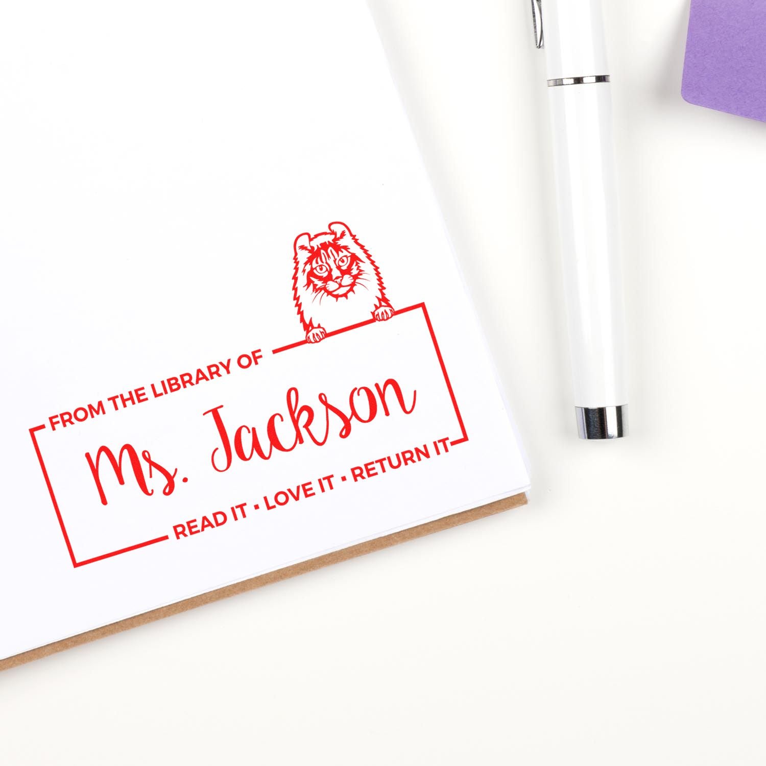 Personalized library rubber stamp with tiger design and From the Library of Ms. Jackson book return imprint on a page.