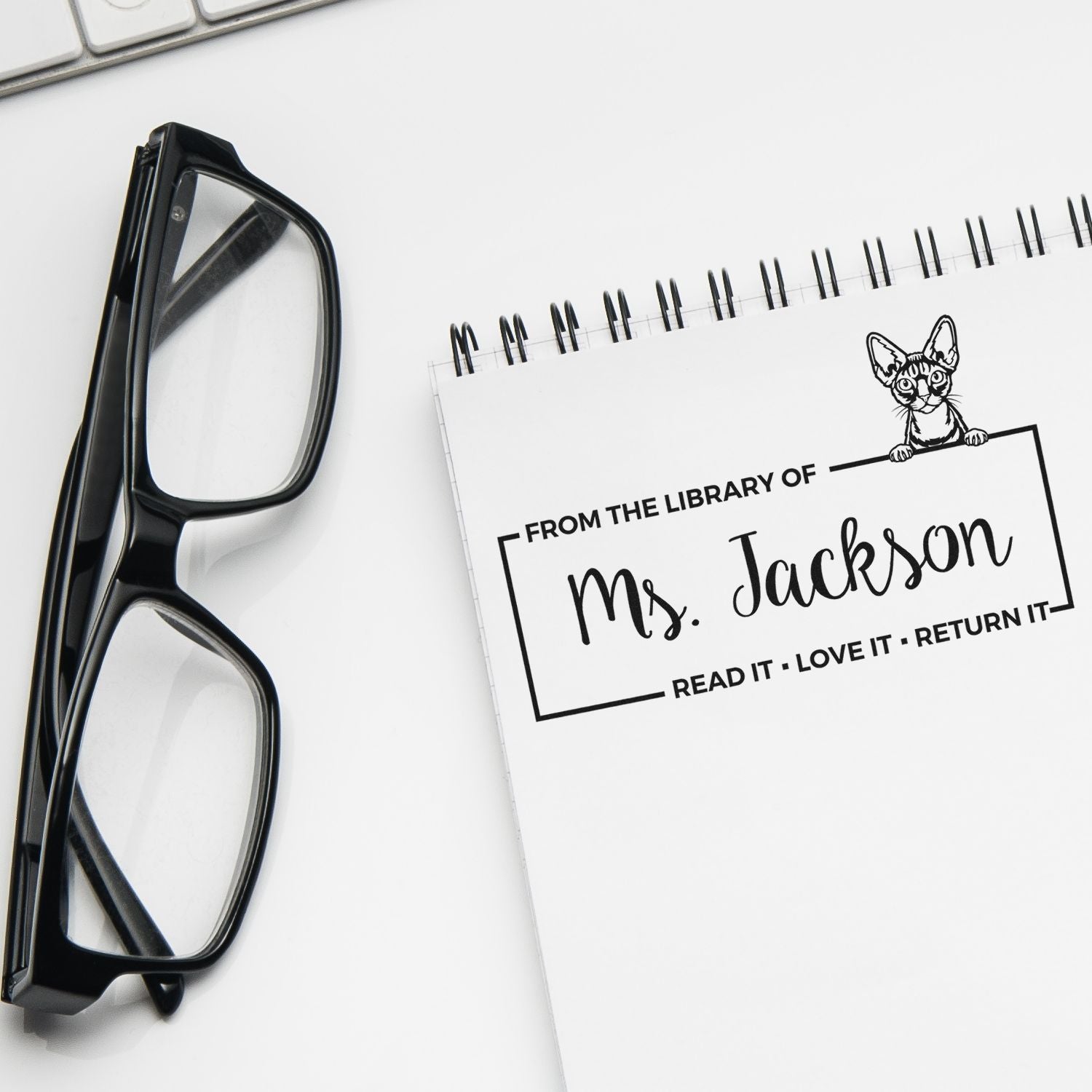 Custom library rubber stamp for books, showing a From the library of Ms. Jackson return reminder on a notebook.