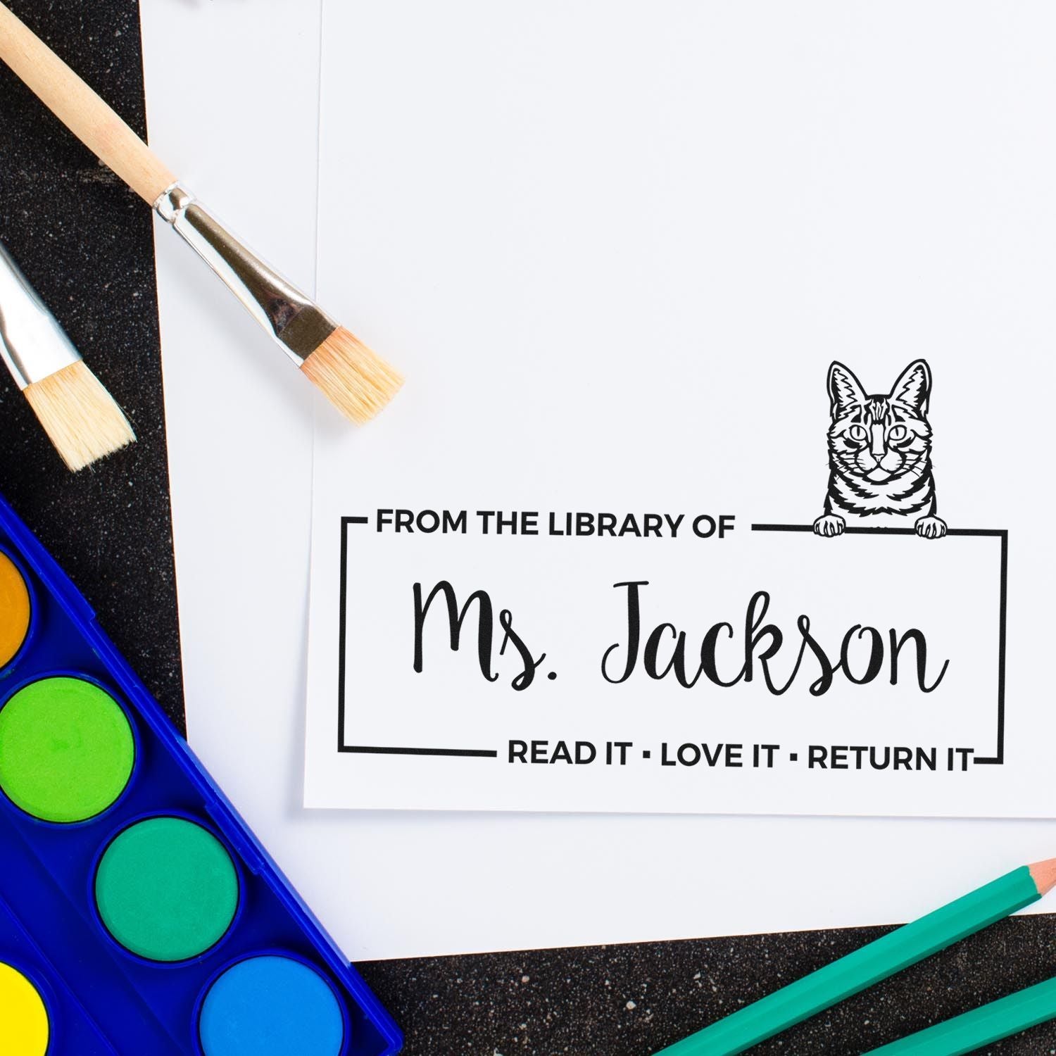Custom rubber library stamp reading From the Library of Ms. Jackson with cat design and art supplies.