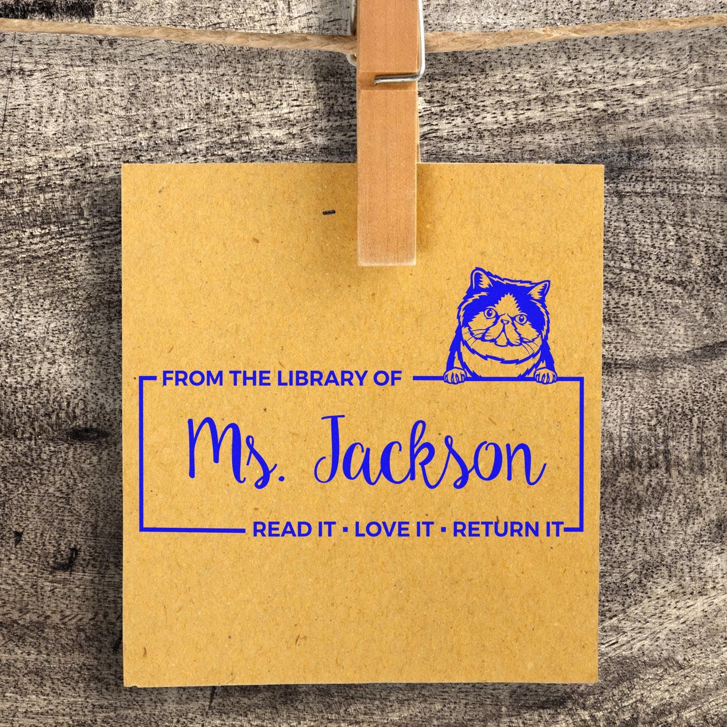 Personalized rubber library stamp with cat design reading From the Library of Ms. Jackson on a clipped note card.