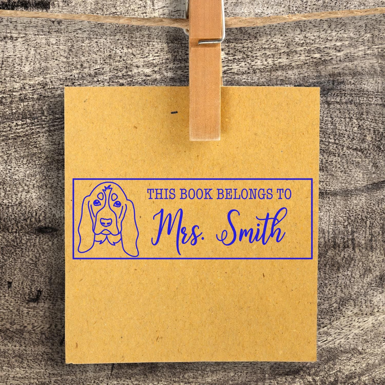 Personalized rubber stamp bookplate for Mrs. Smith with dog illustration and This Book Belongs To text on kraft tag.