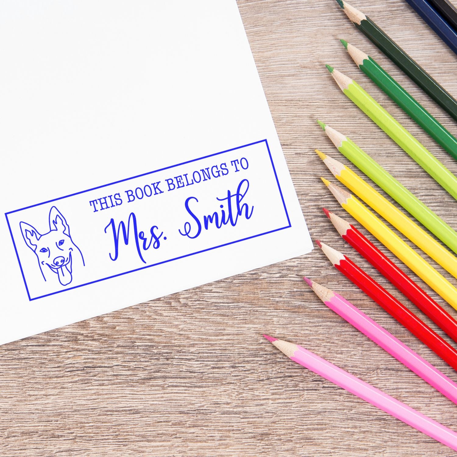 Custom rubber stamp bookplate for Mrs. Smith with dog design, shown on paper beside colorful pencils.
