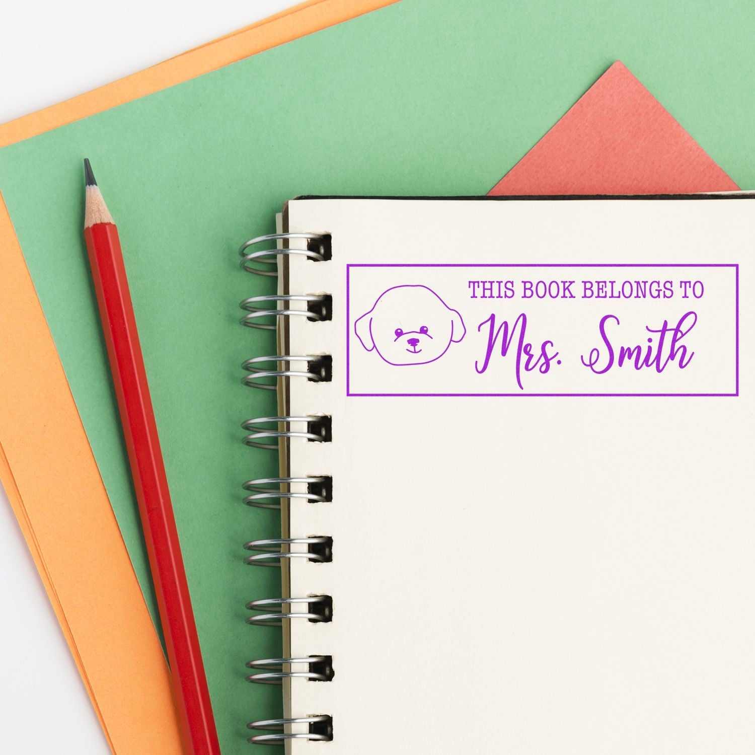 Personalized book stamp reading This Book Belongs to Mrs. Smith with dog icon on a spiral notebook.