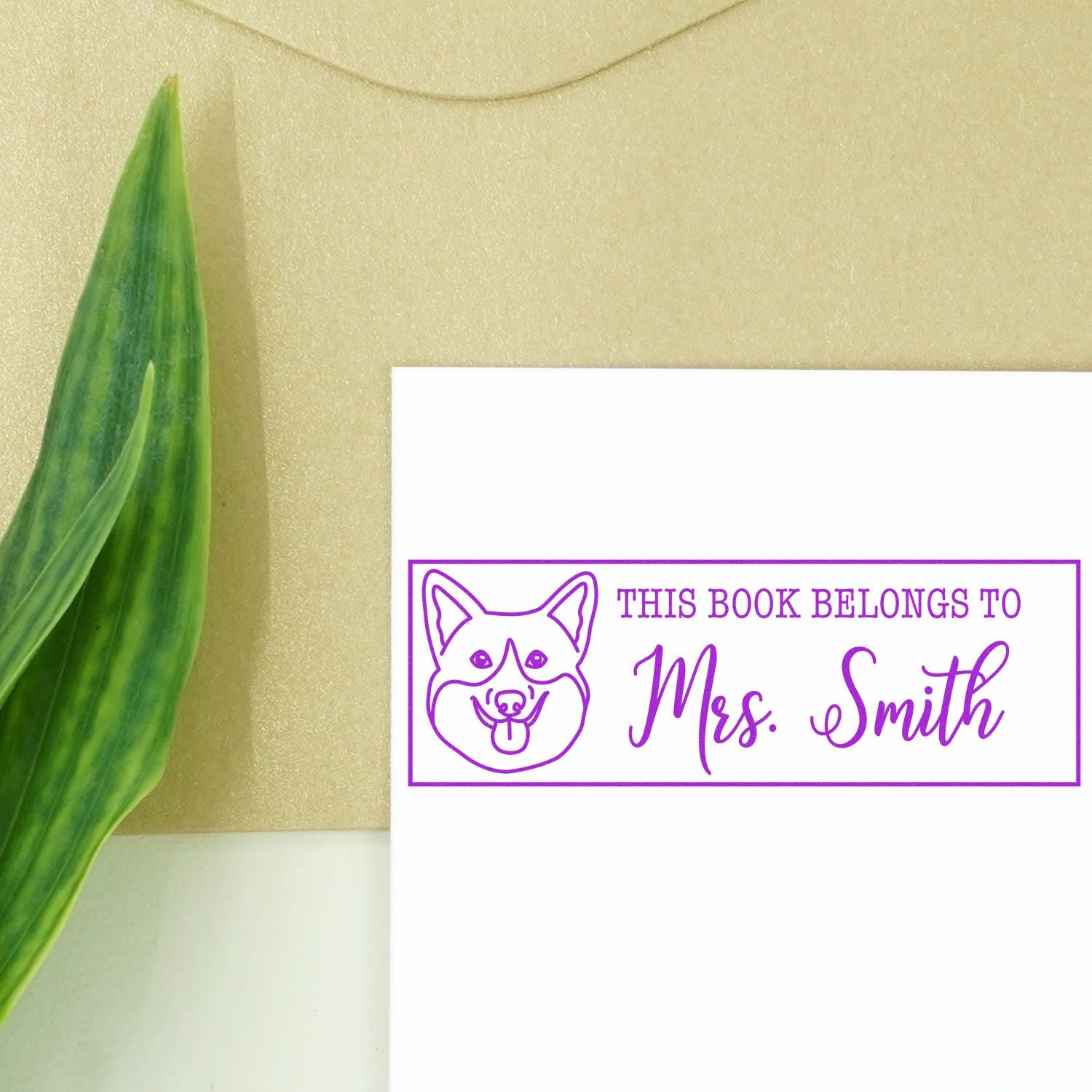Personalized rubber book stamp with dog illustration, reading This Book Belongs to Mrs. Smith in purple ink.
