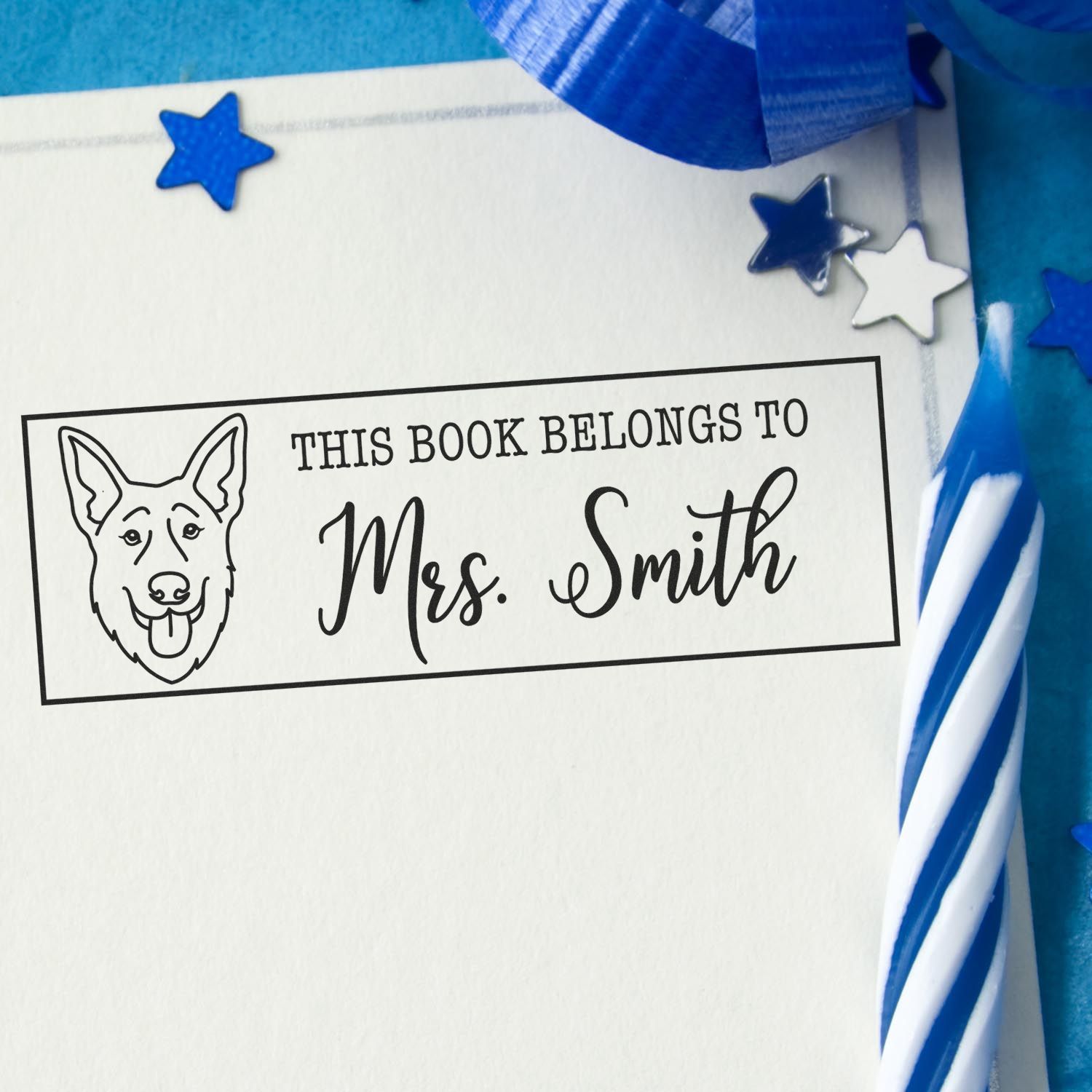 Personalized book rubber stamp with dog illustration and This Book Belongs to Mrs. Smith ex libris design in blue.